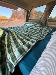 RV rental's cozy car camping bed, with a plaid quilt, offers stunning desert views. Perfect for your next road trip!. Chevrolet Tahoe 2002