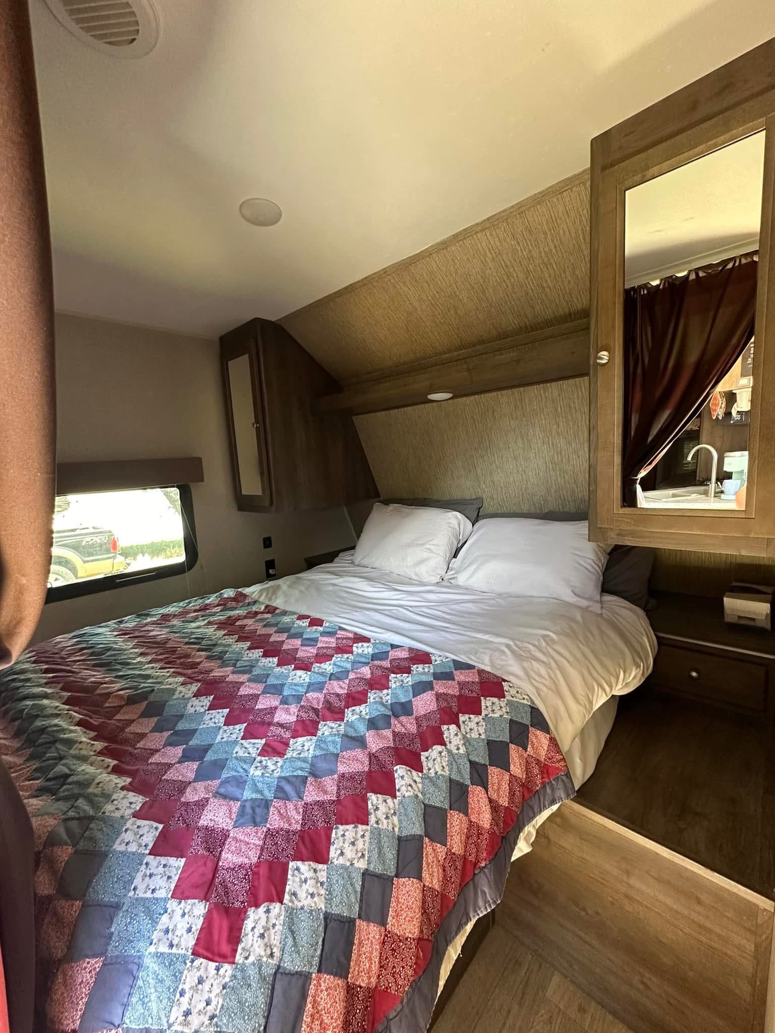 Experience comfort in this RV rental bedroom featuring a colorful patchwork quilt, overhead cabinets, and a mirrored door revealing a sink area.. Dutchmen Coleman Lantern 2017