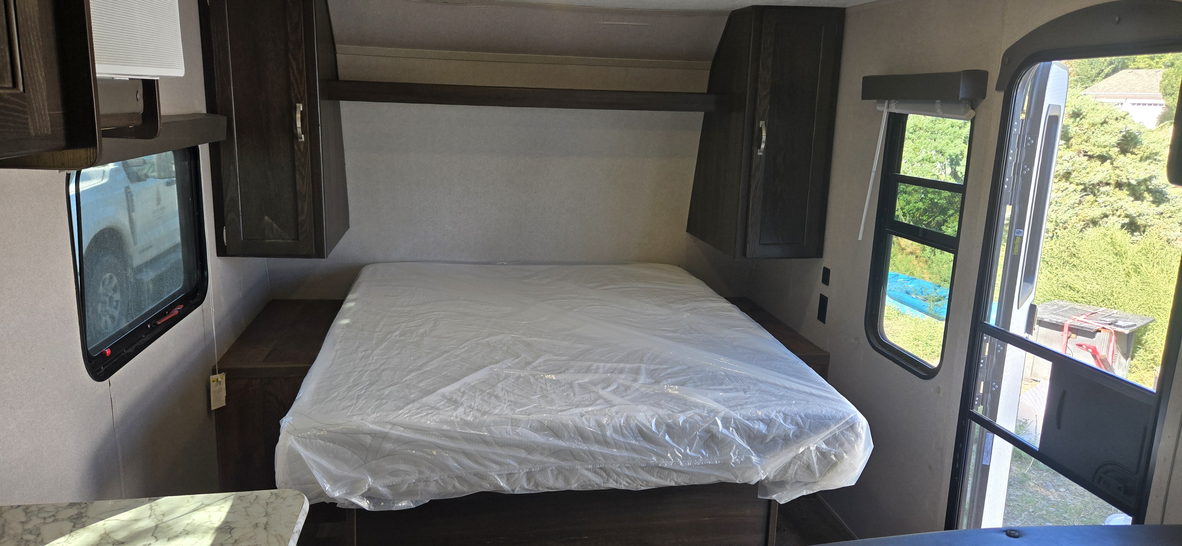 New RV rental bedroom: bed with protective plastic, dark wood cabinets, and bright windows.. Keystone RV Springdale 2019