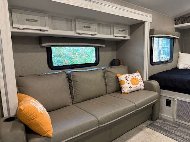 Enjoy the comfy living space of this RV rental, featuring a gray couch, festive fall pillows, and a cozy sleeping area.. Forest River Rockwood Geo Pro 2021