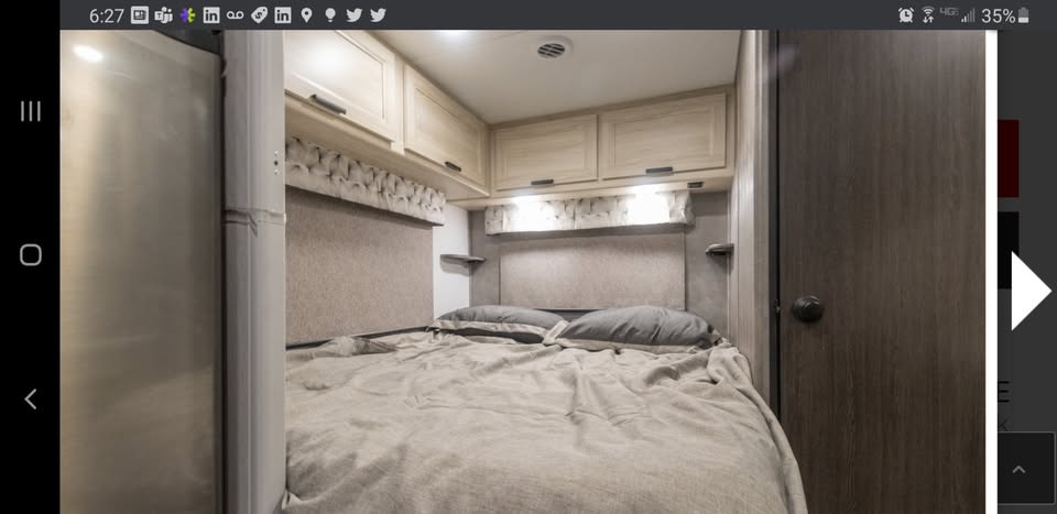 This cozy RV rental bedroom features a comfortable bed with light bedding, overhead cabinets, and warm lighting.. Forest River SLE 2021