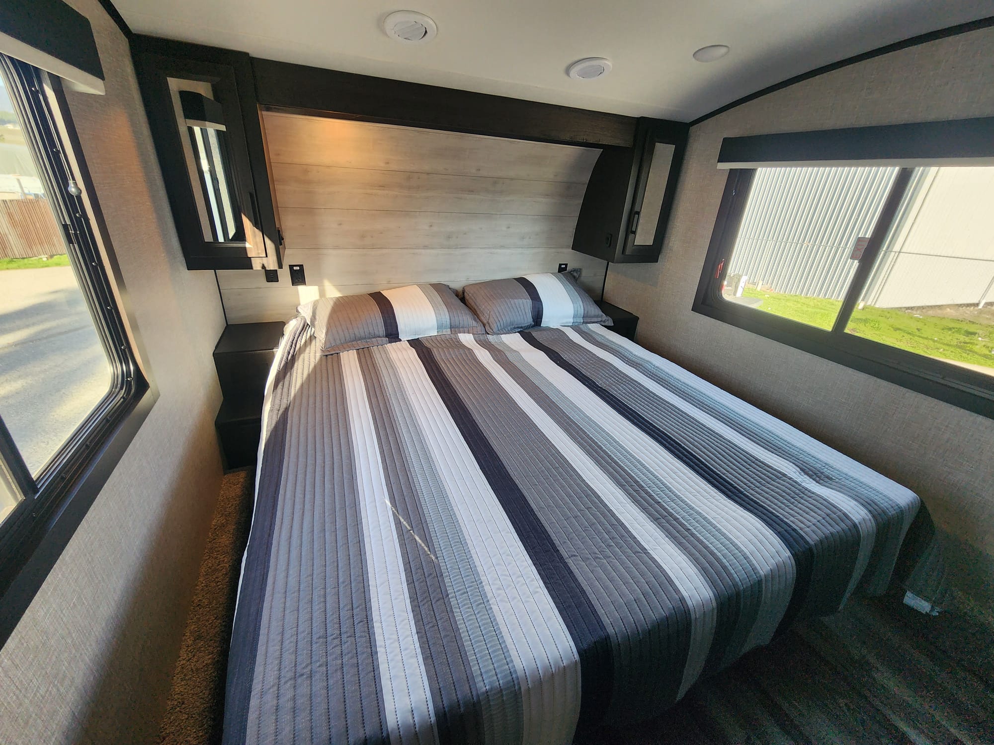 Cozy bedroom in an RV rental featuring a striped bed, wood headboard, and windows. Perfect for your next adventure.. Jayco Eagle HT 2023
