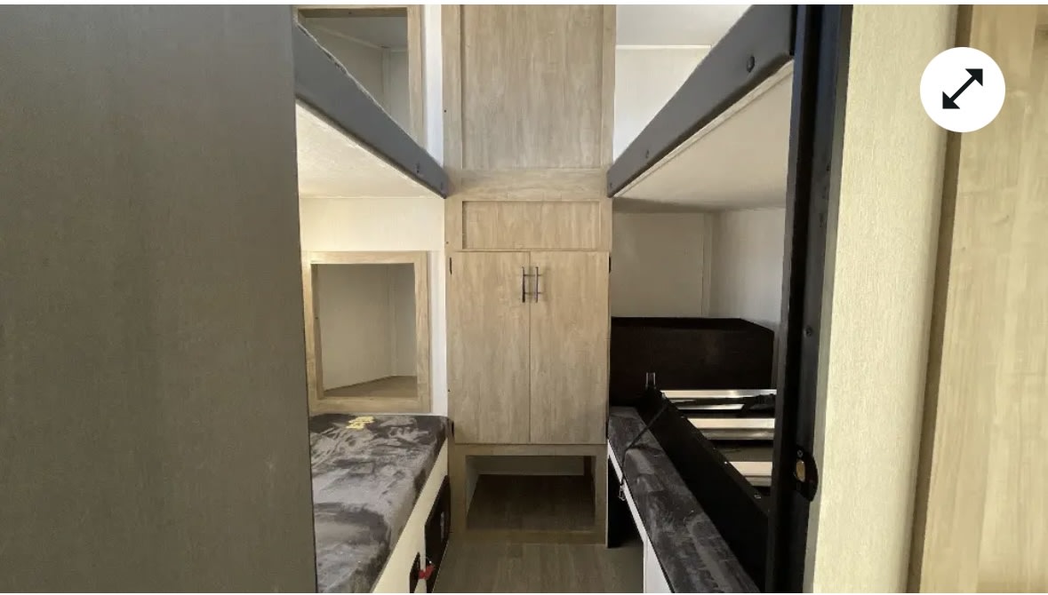 RV rental bunk bed setup: a central wooden cabinet divides two sets of bunks, featuring dark mattresses.. Forest River Campsite reserve 39GB 2025