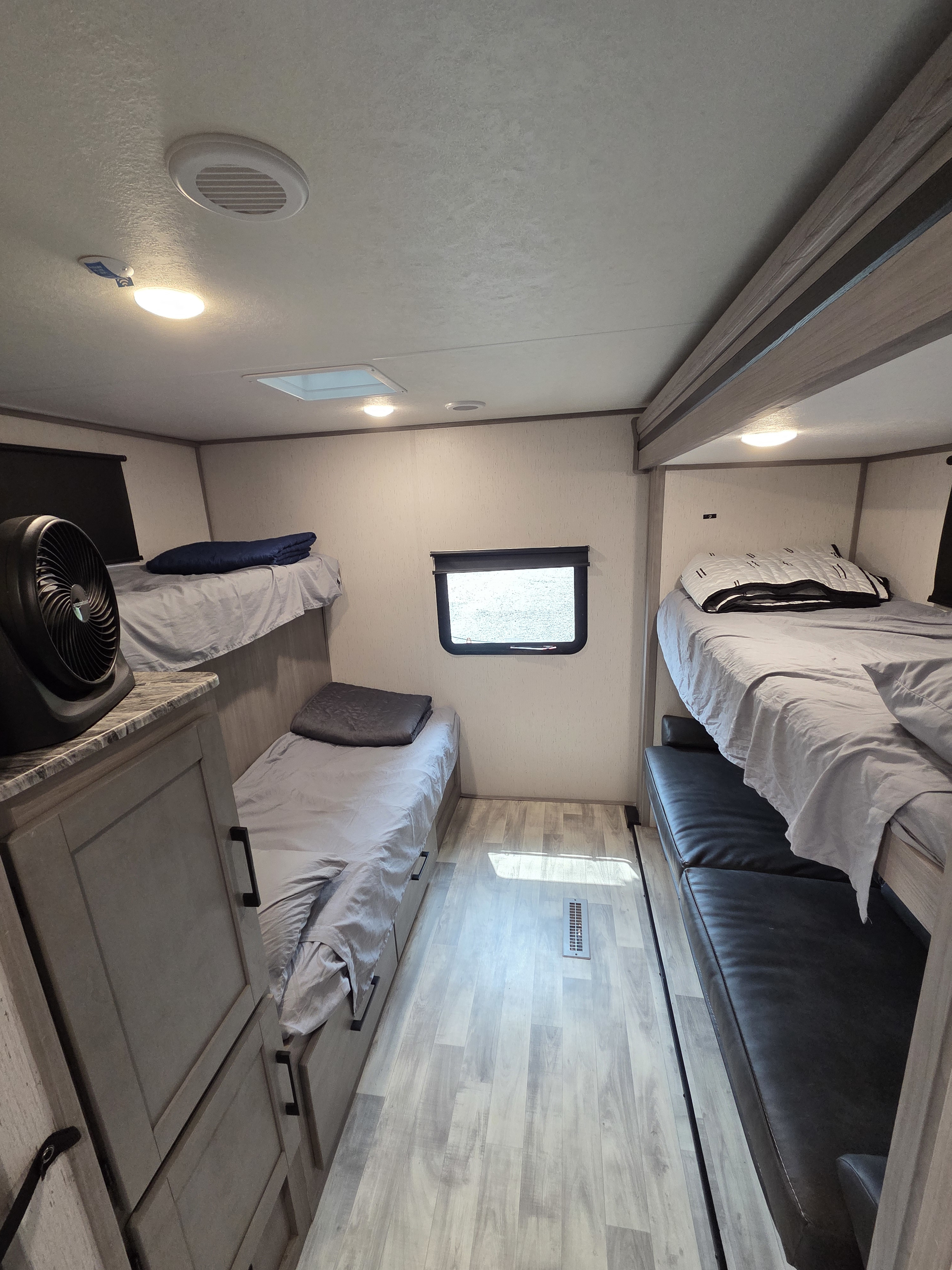 This rv rental bunkhouse with stacked bunk beds, a lower sofa bed, window, and storage cabinets, providing a compact sleeping area.. Dutchmen Kodiak Ultra Lite 2023