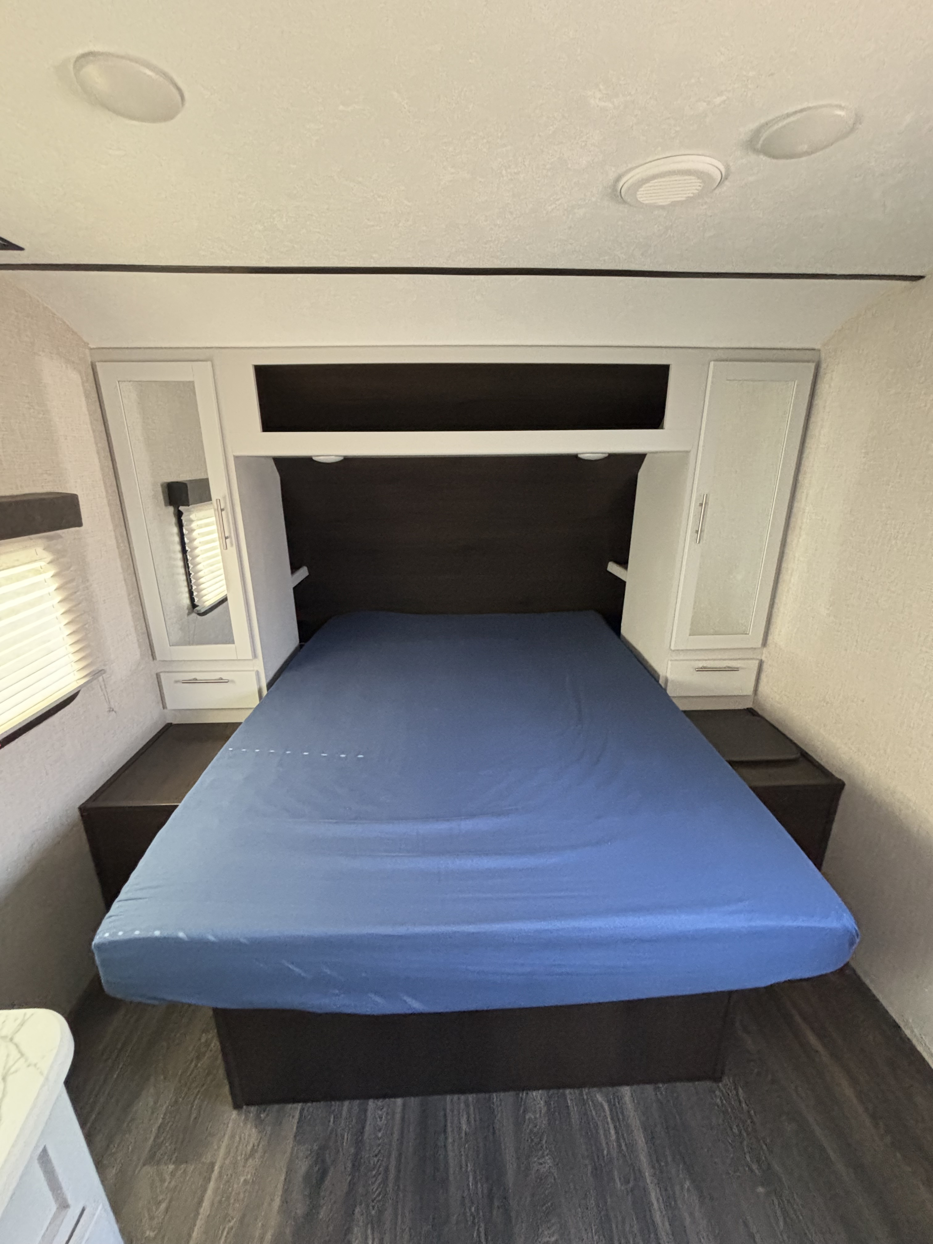 Compact RV rental bedroom featuring a blue bed, integrated overhead & side storage, and ceiling lights, ideal for travel.. Keystone RV Bullet Ultra Lite 2021