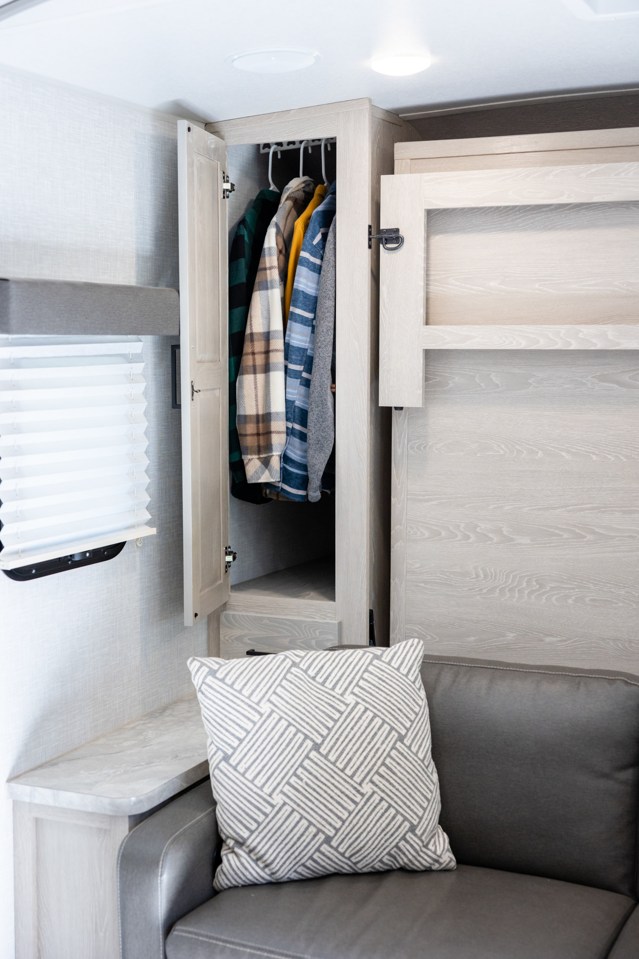 RV rental's interior: An open closet with clothes, light-toned cabinetry, and a gray sofa with a patterned pillow.. Forest River Rockwood Mini Lite 2021