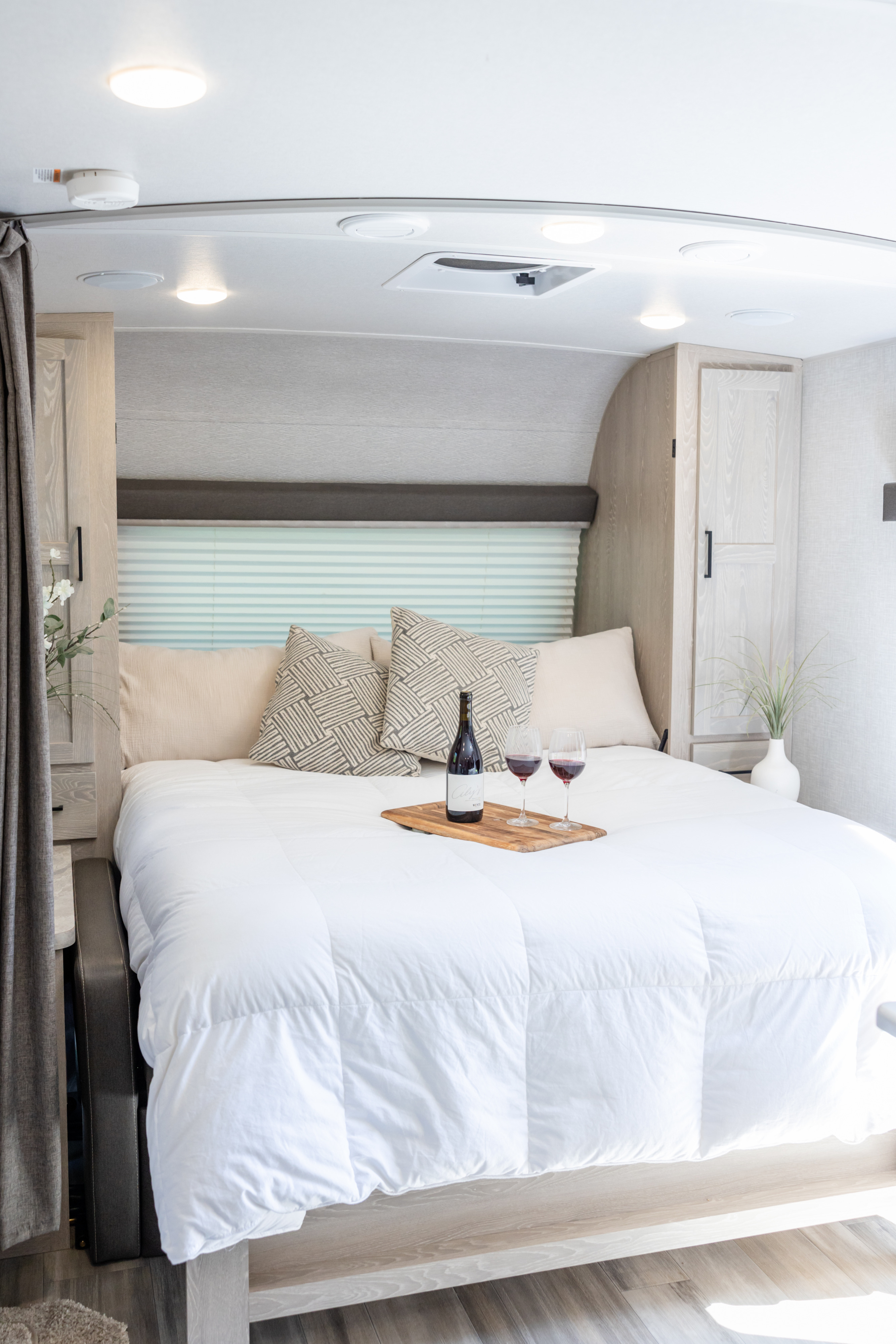 Relaxing rv rental bedroom with a fresh white comforter, decorative pillows, wine on a tray, and light wood cabinetry.. Forest River Rockwood Mini Lite 2021