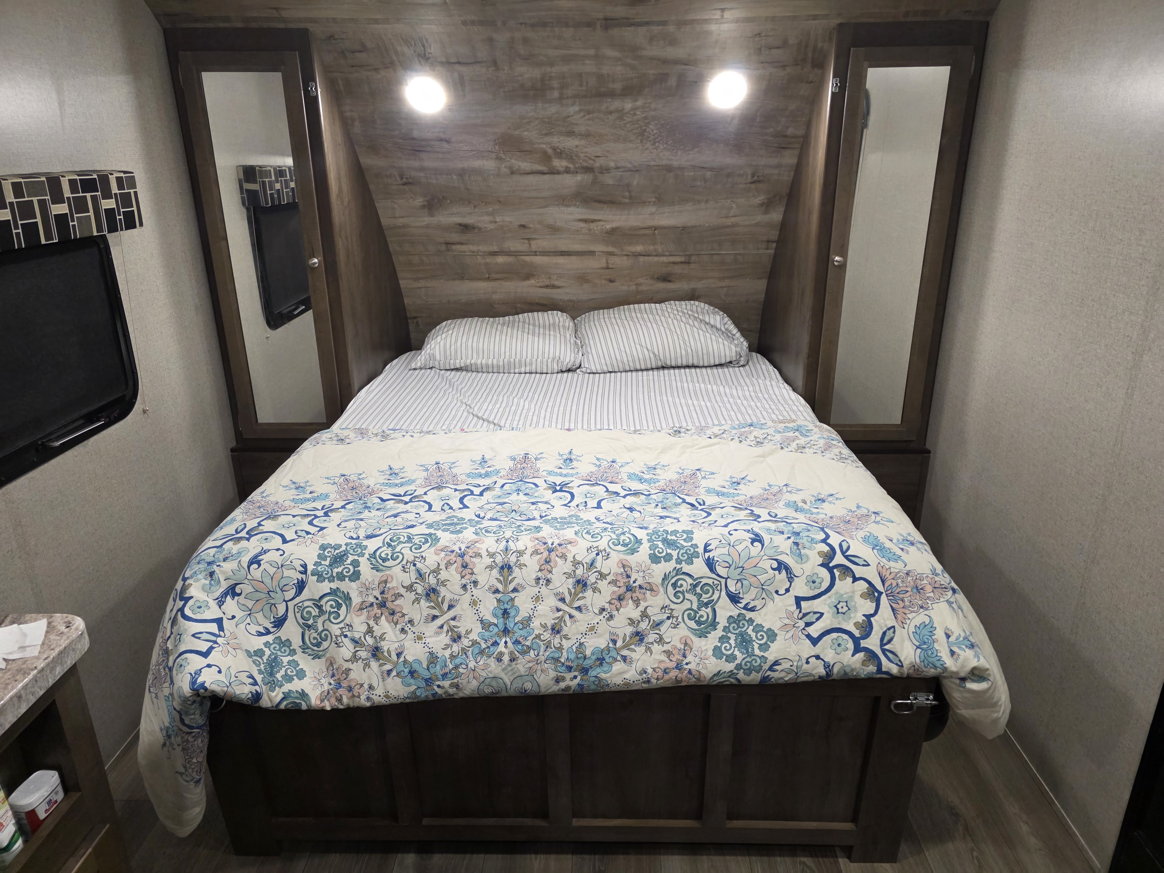 Cozy RV rental bedroom featuring a bed with a floral duvet, striped pillows, and mirrored storage on both sides.. Dutchmen Coleman Light LX 2019