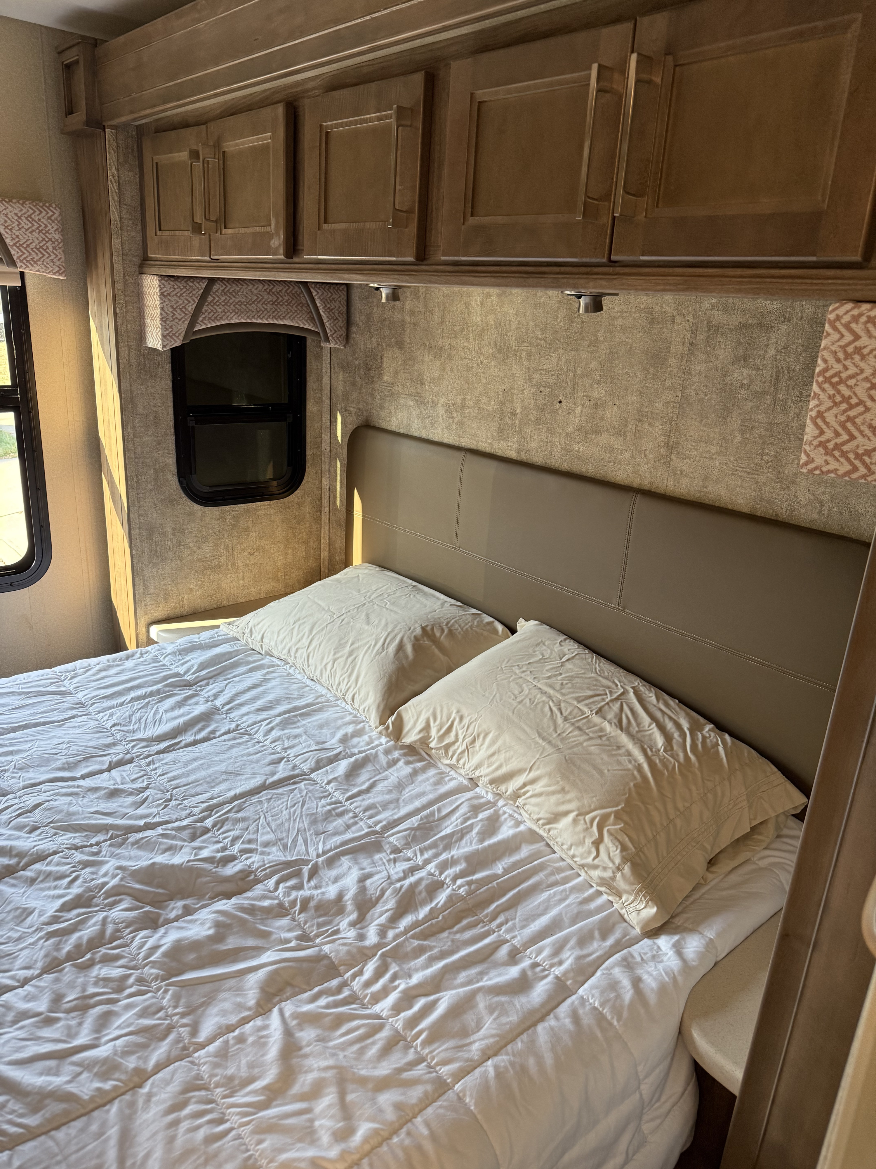 Inside a comfortable RV rental bedroom, featuring a neatly made bed with a padded headboard and functional overhead cabinets.. Jayco Greyhawk Prestige 2018