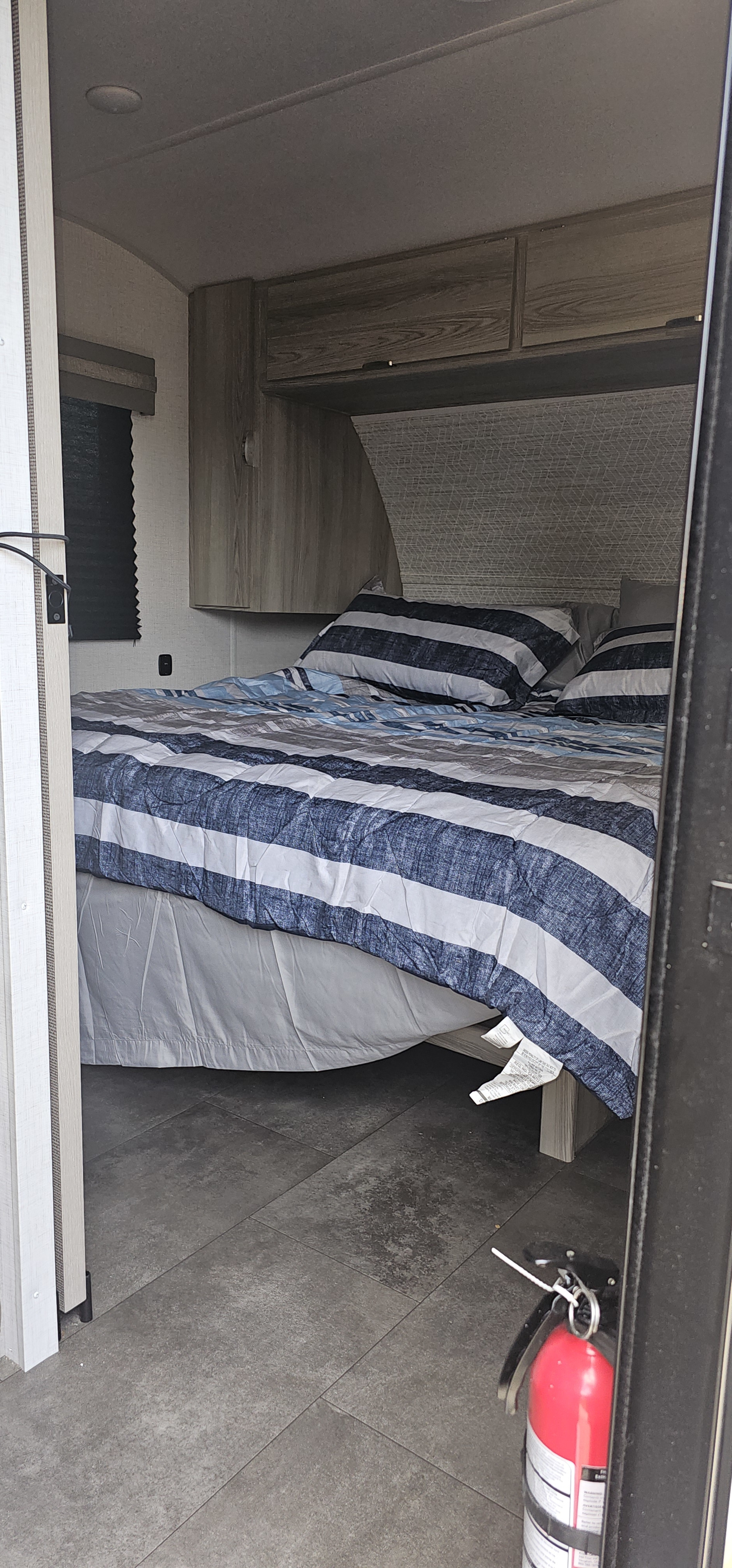 Cozy rv rental bedroom interior with blue striped bedding, overhead cabinets, and a fire extinguisher on the floor for safety.. Forest River Salem FSX 2024