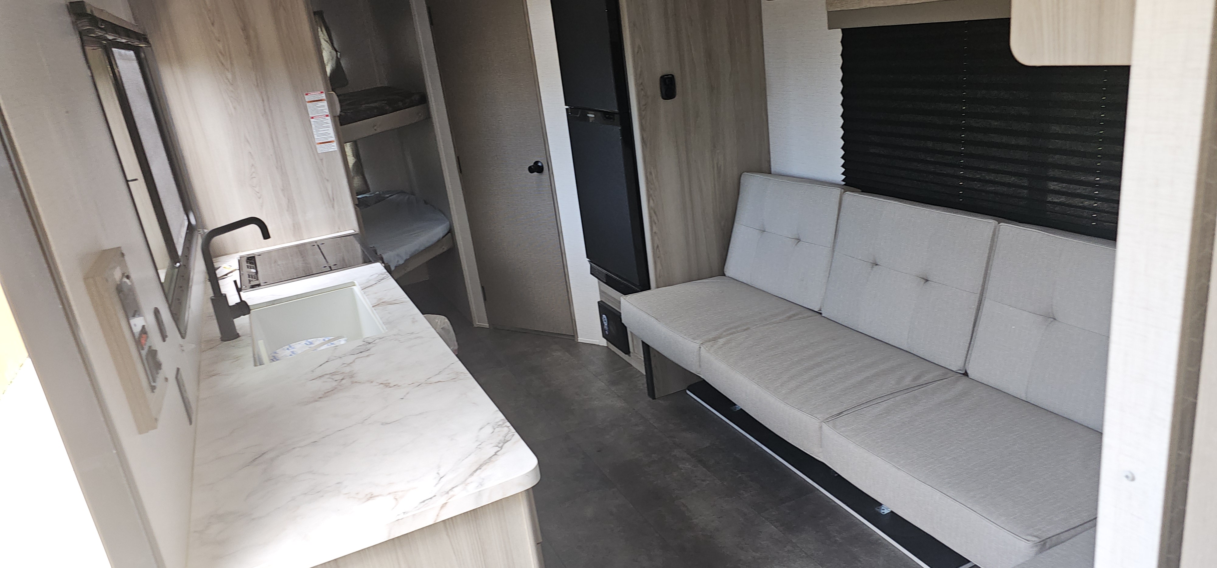 This RV rental interior features a compact kitchen counter with a sink, a grey sofa, refrigerator, and bunk beds.. Forest River Salem FSX 2024
