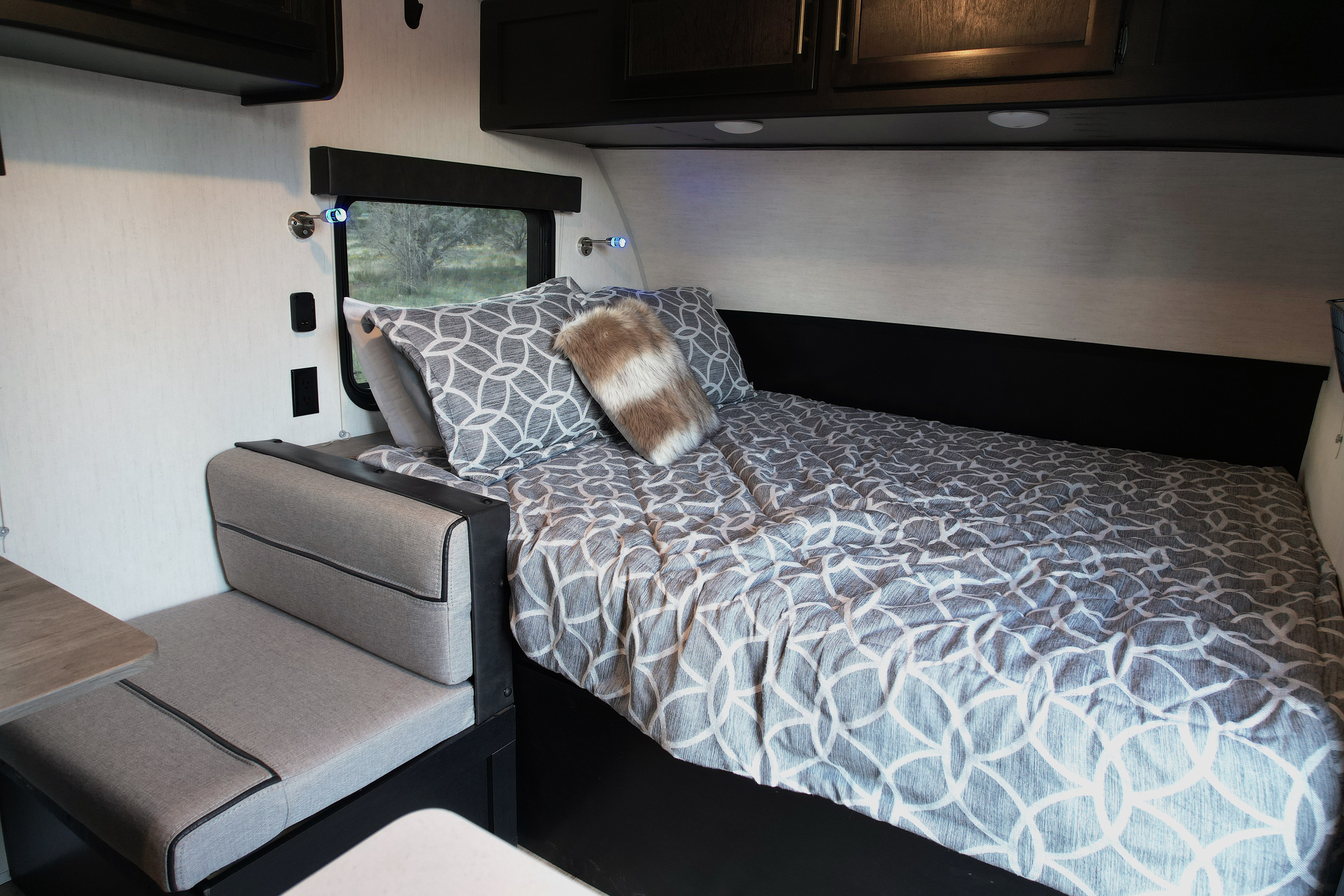 Cozy rv rental bed area with patterned bedding, a window view, reading lights, and adjacent dinette seating.. Forest River Cherokee Wolf Pup Black Label 2022
