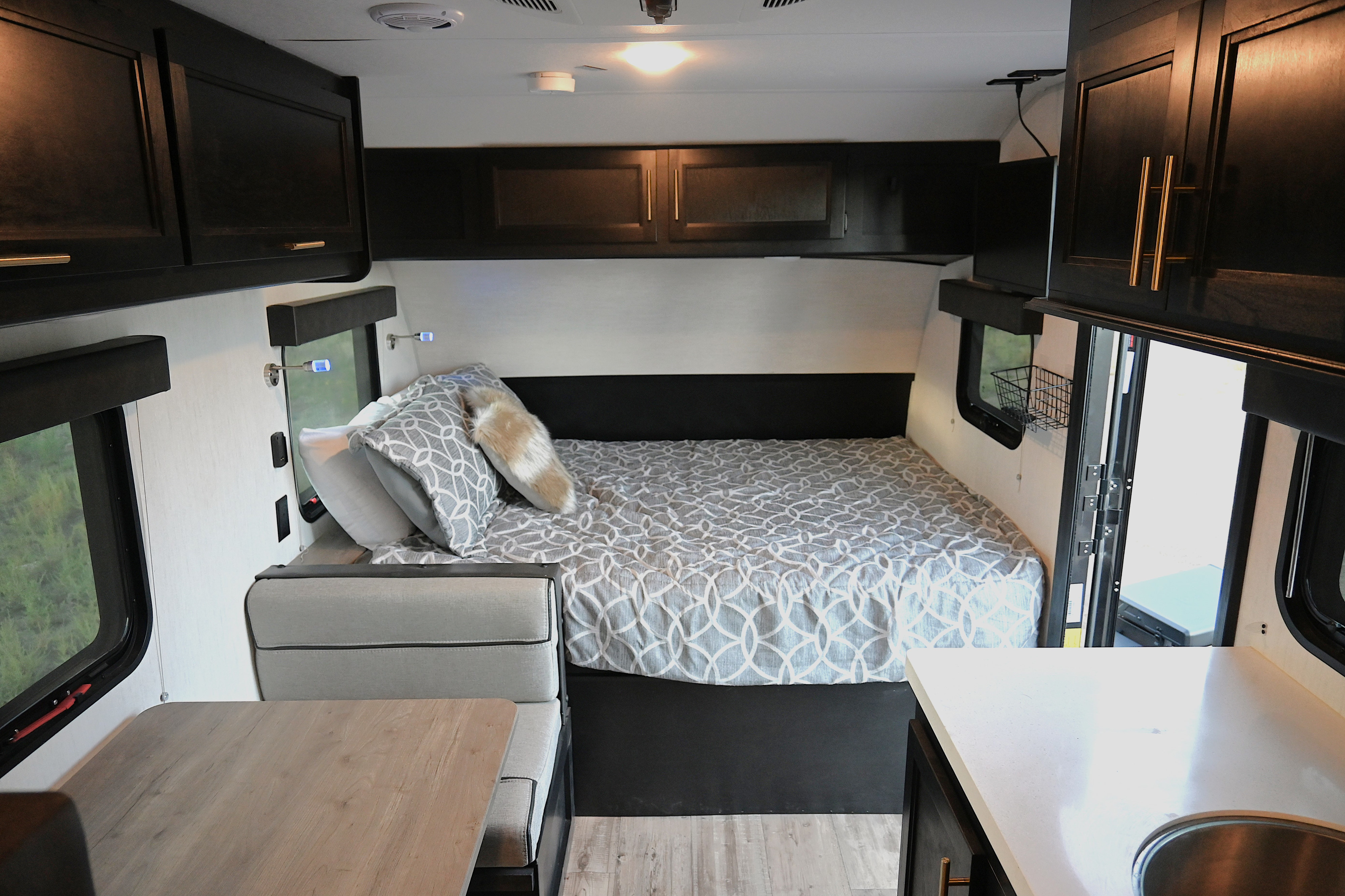 This clean rv rental interior features a cozy bed, dining area, and compact kitchenette with dark cabinets and light countertops.. Forest River Cherokee Wolf Pup Black Label 2022