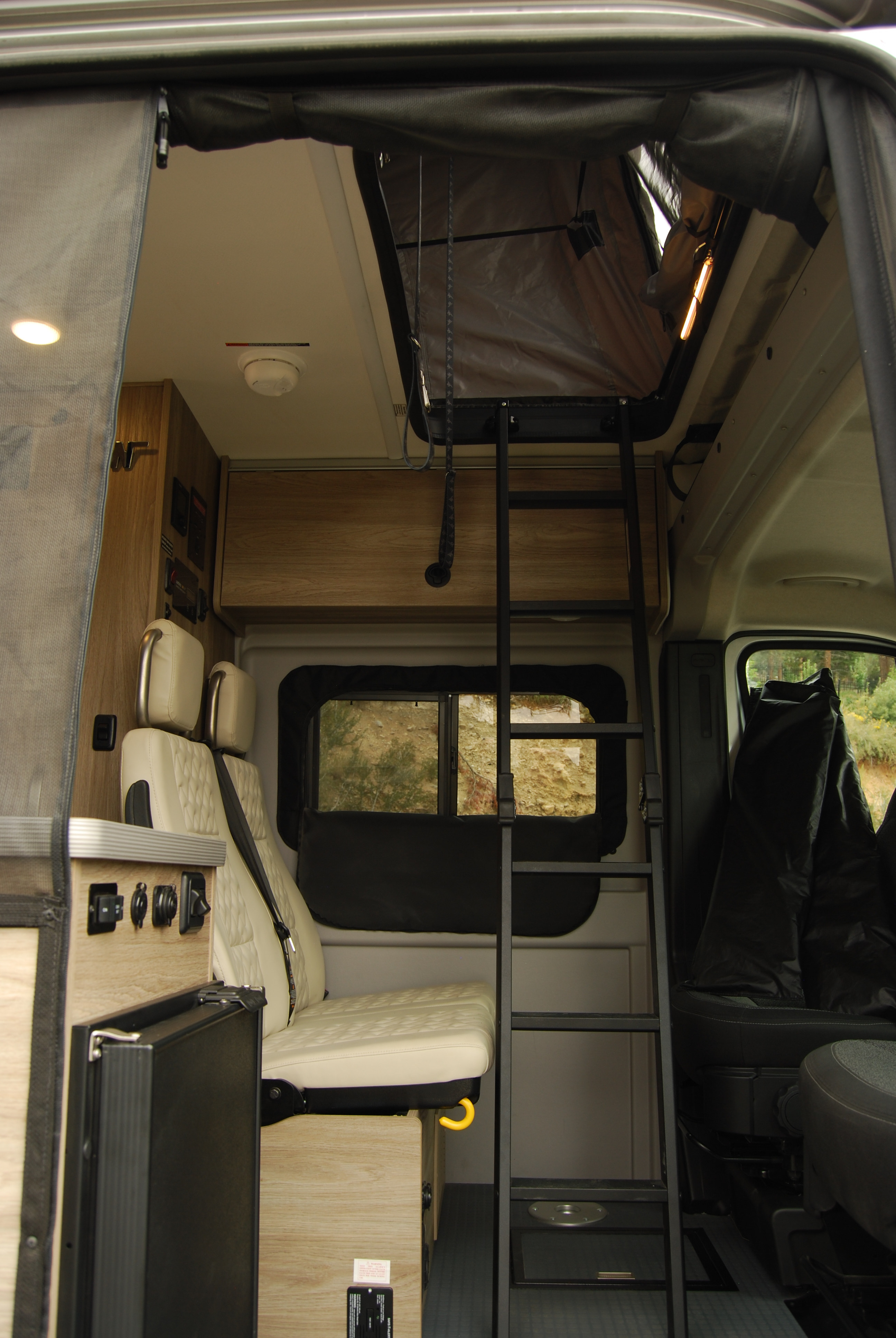 RV rental interior showing a ladder to a pop-top bed, plush seating, and controls for a comfortable camper experience.. Winnebago Soilis 2025
