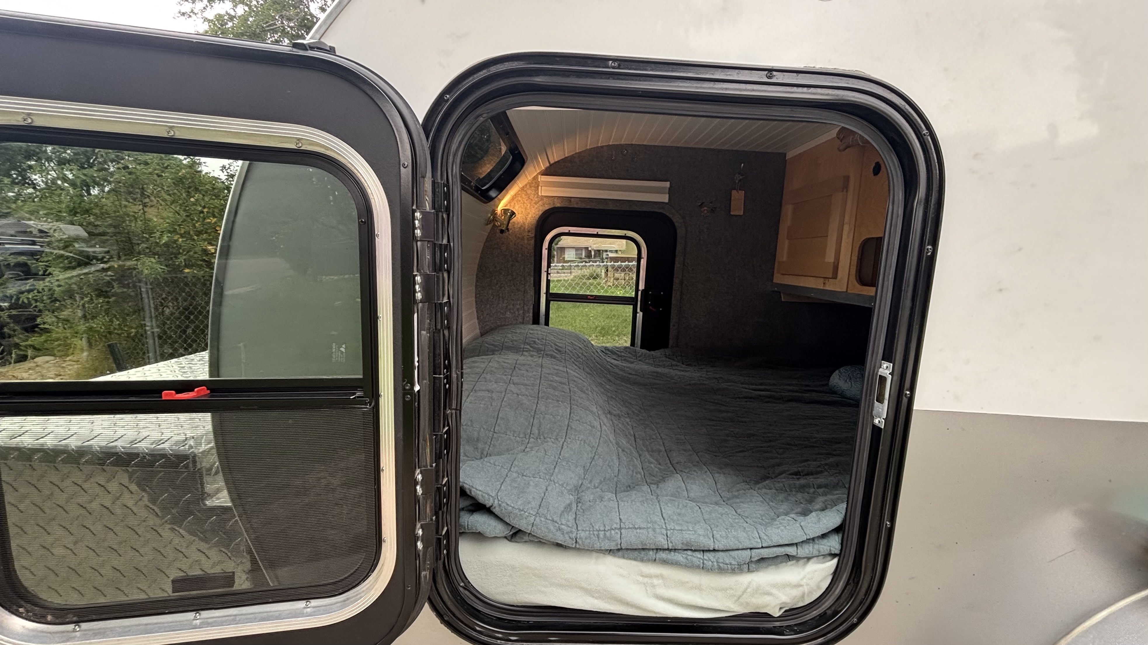 Cozy rv rental interior with a comfy bed visible through the open door of a compact camper.. American Teardrop Merlin 2016