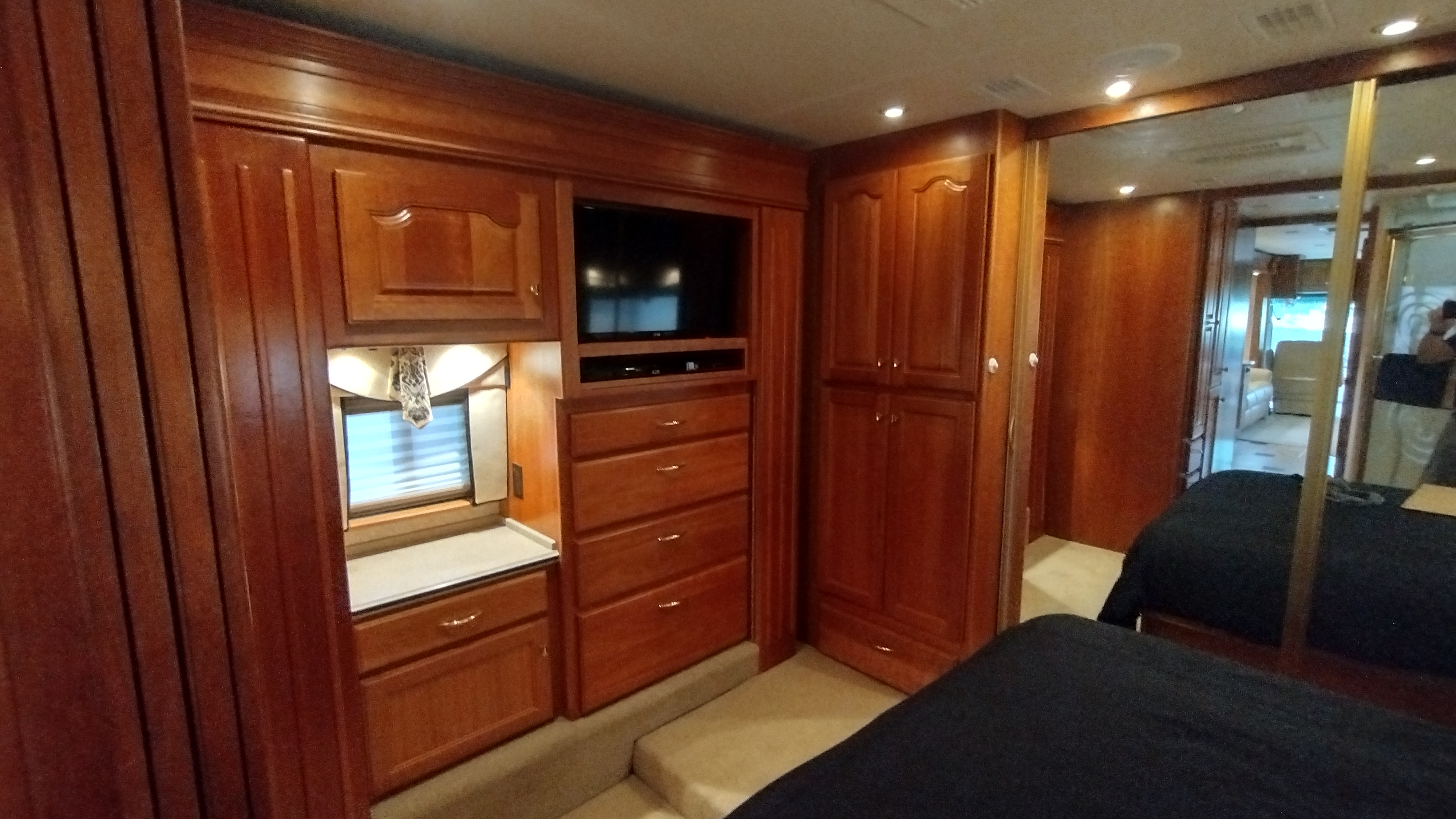 Luxurious RV rental bedroom featuring rich wooden cabinets, a built-in TV, drawers, and a cozy bed reflected in mirrors.. Country Coach Allure 470 2005