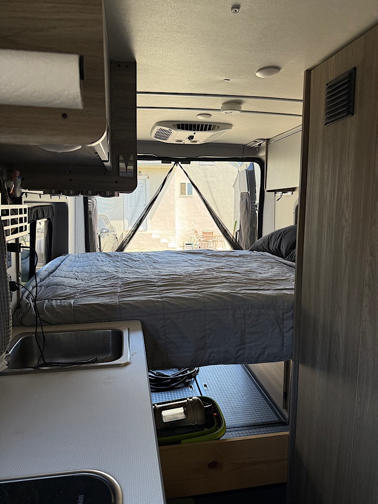 This RV rental interior features a comfortable rear bed, kitchen with sink, overhead AC, and a bright view through the back mesh doors.. Winnebago Solis 2023