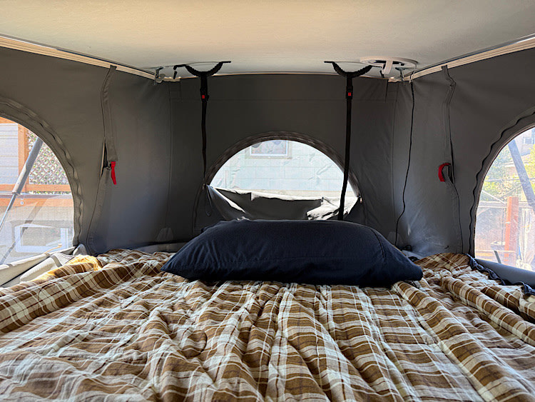 Cozy RV rental pop-top camper interior: a neatly made bed with a plaid comforter under a panoramic view.. Winnebago Solis 2023