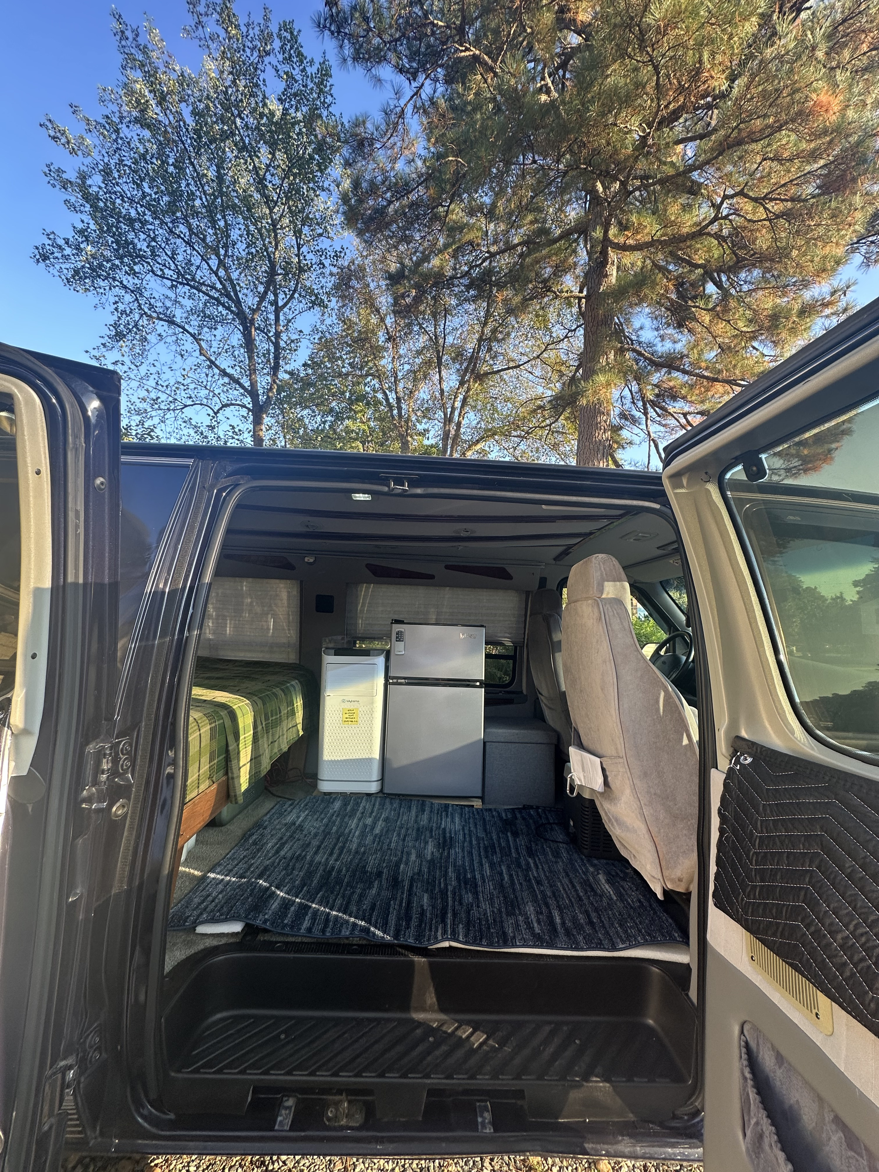 This cozy camper van rv rental shows the interior: bed, mini-fridge, and air purifier, ready for comfortable travel.. Ford Econoline 150 1999