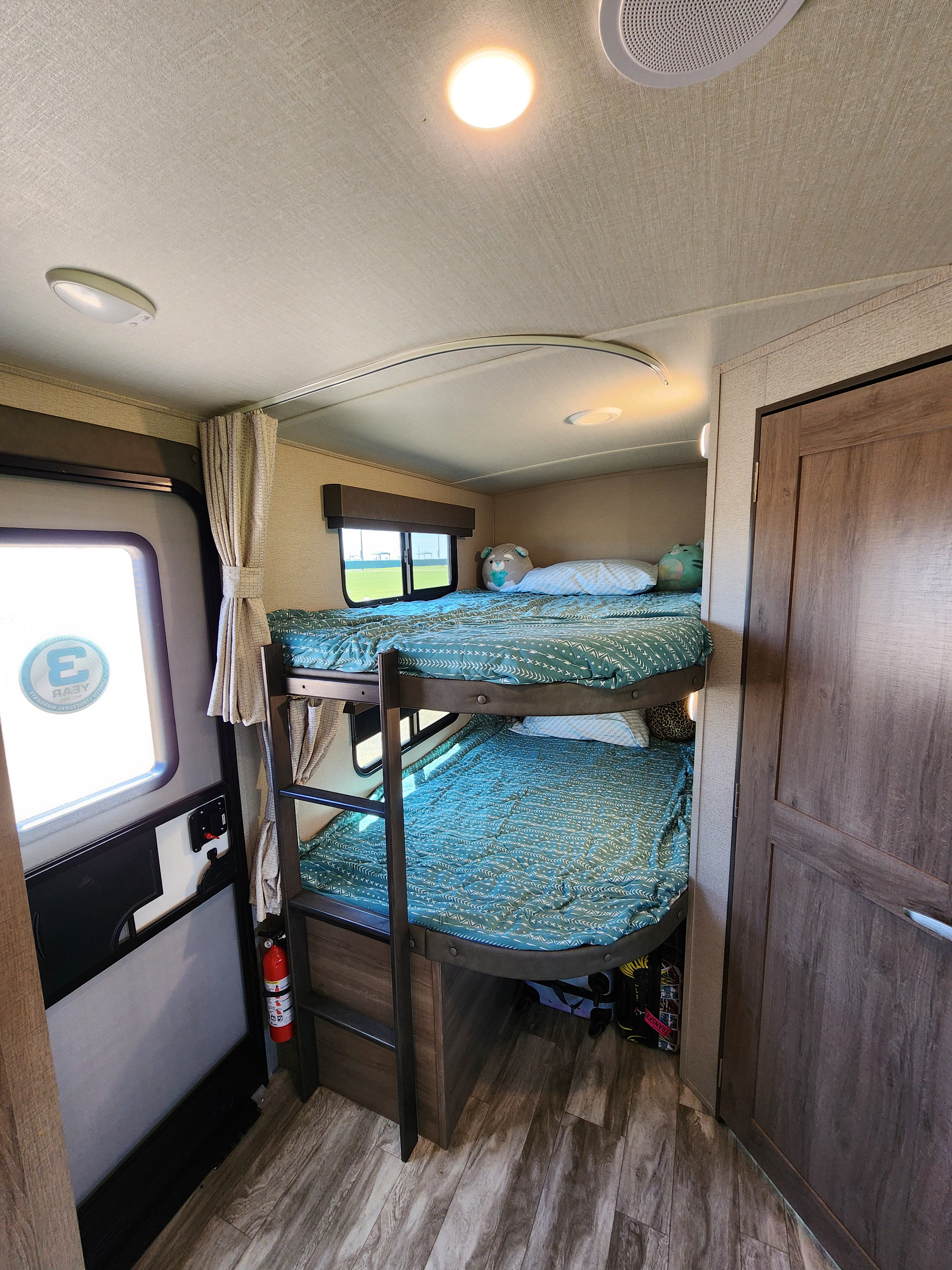 RV rental bunk beds: twin beds with teal bedding, a window, and a fire extinguisher in a compact sleeping area.. Grand Design Imagine 2022