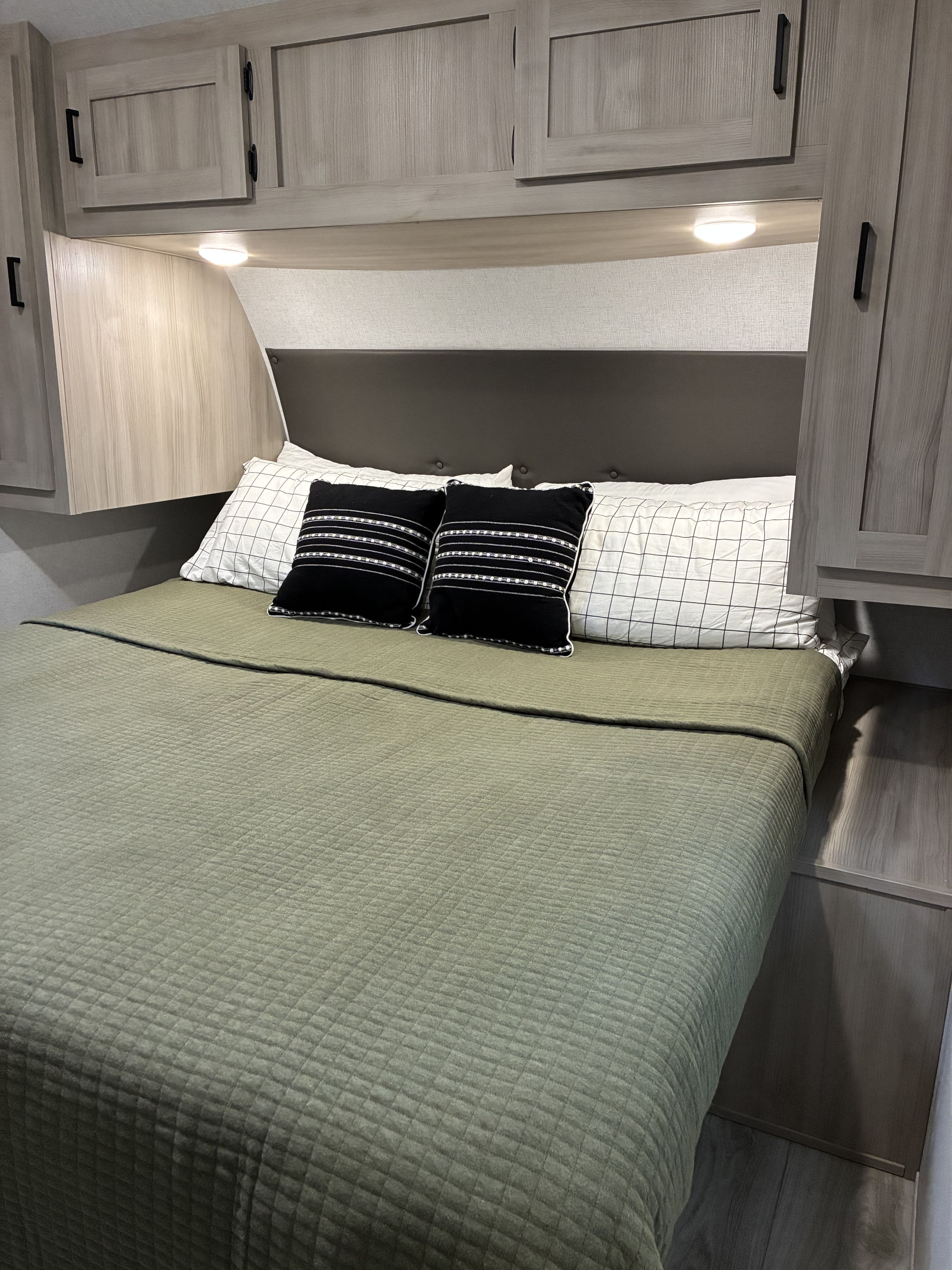 Cozy RV rental bedroom with a comfy bed, green quilt, stylish pillows, and overhead storage for a pleasant stay.. East To West Della Terra 2025