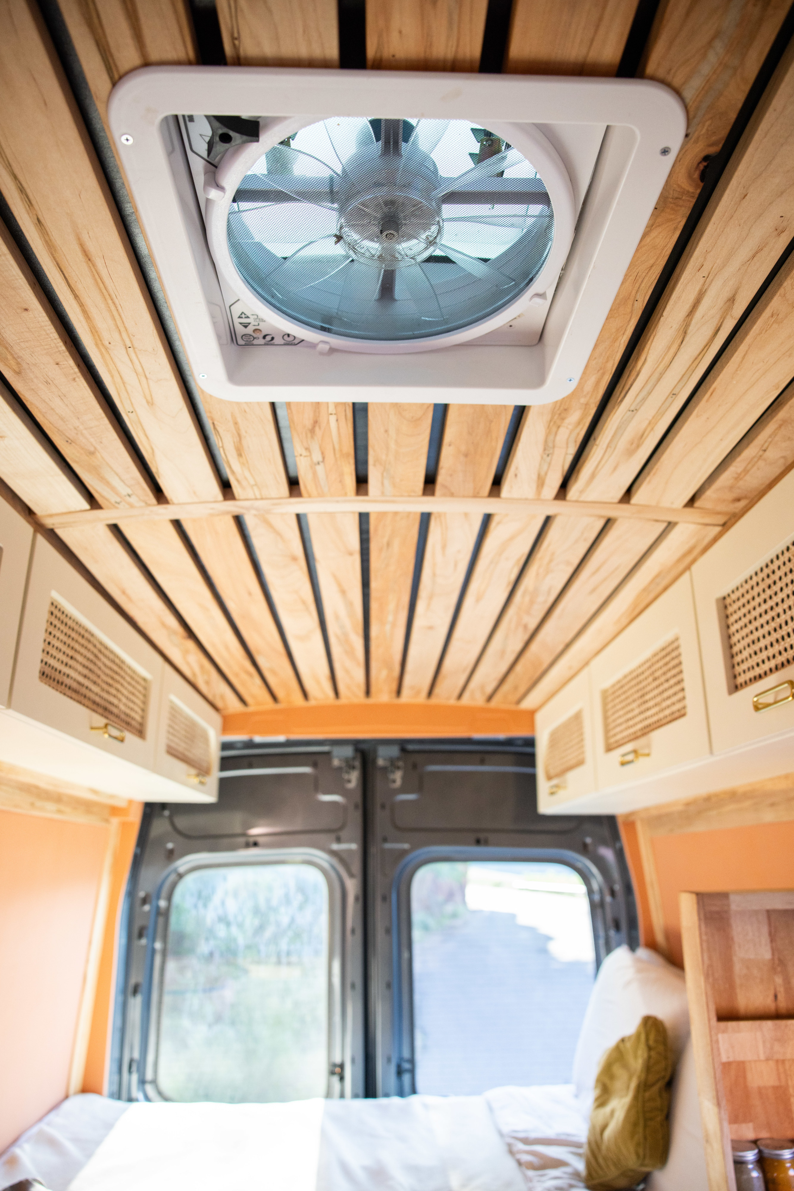 Looking up inside an RV rental: wood-slat ceiling, rooftop vent, overhead cabinets, and bed in a cozy camper van.. Ford Transit 2023