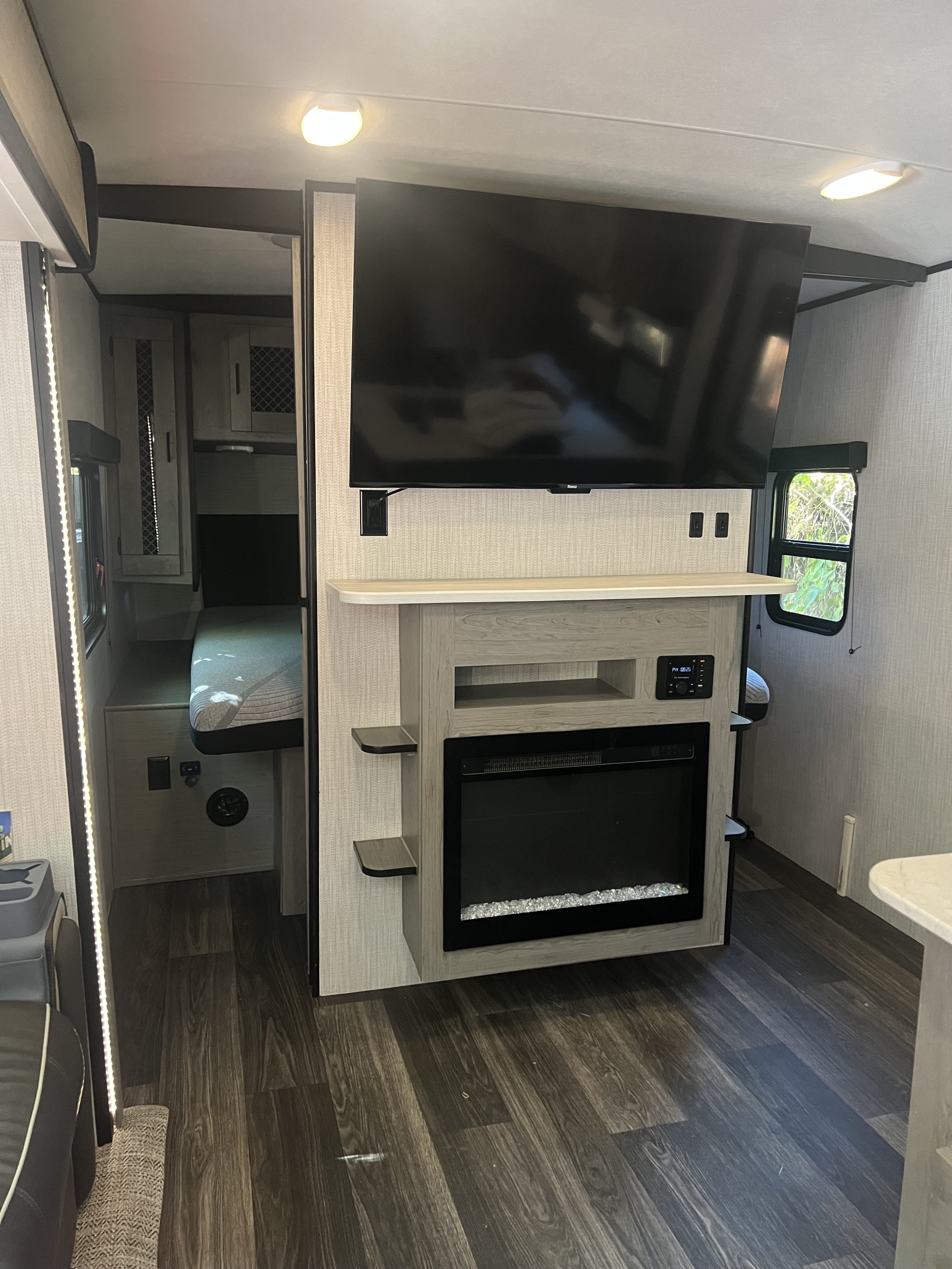 Modern **rv rental** living area with a large TV, electric fireplace, and cozy bunk beds. Dark wood floors and bright lighting enhance comfort.. Heartland RVs Mallard 2022