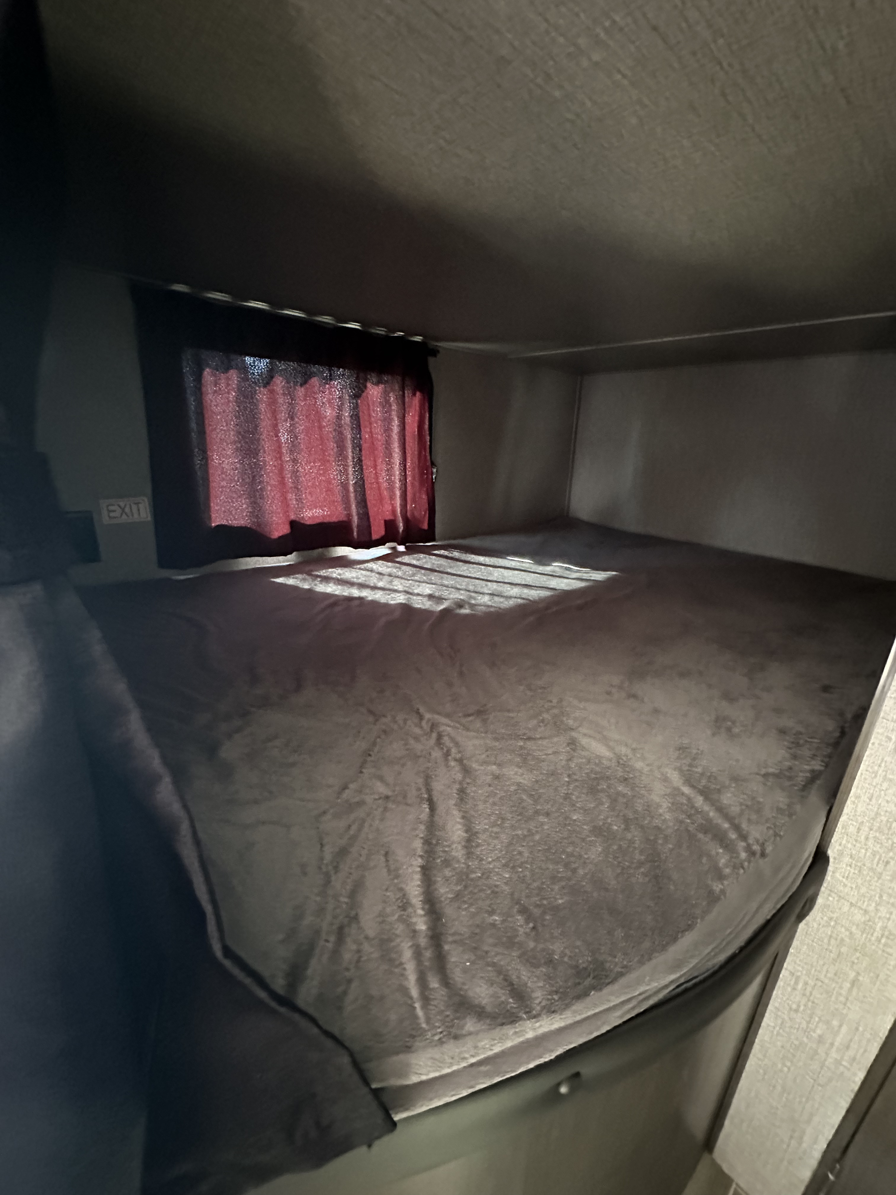 Inside an rv rental: a dark bunk bed with a red curtained window, an "EXIT" sign, and light creating patterns on the bedding.. Jayco Jay Flight SLX 2021