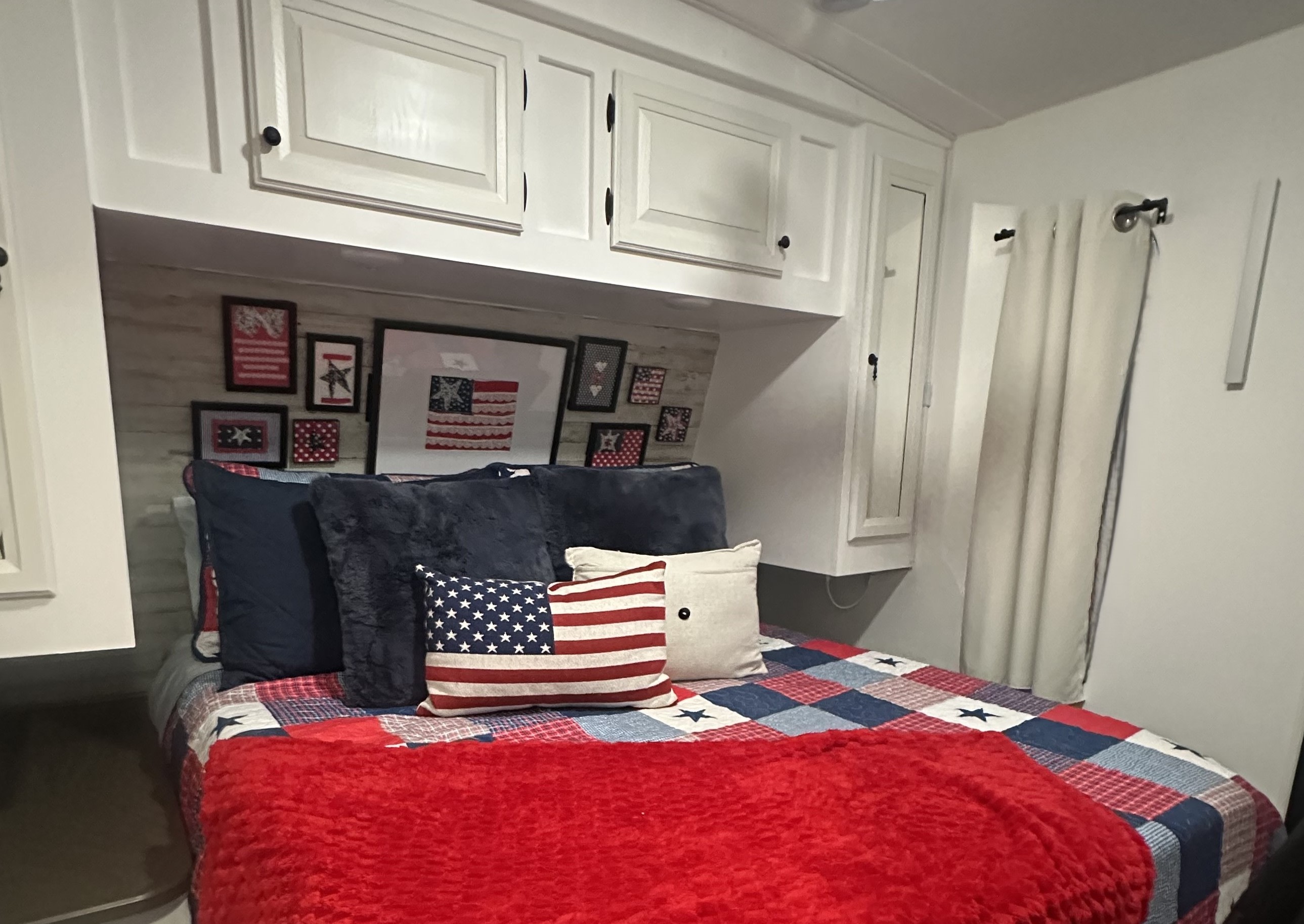 Cozy patriotic RV rental bedroom with a red, white, and blue quilt, throw, pillows, and framed flag art above the bed.. Jayco Eagle 298RLDS 2013