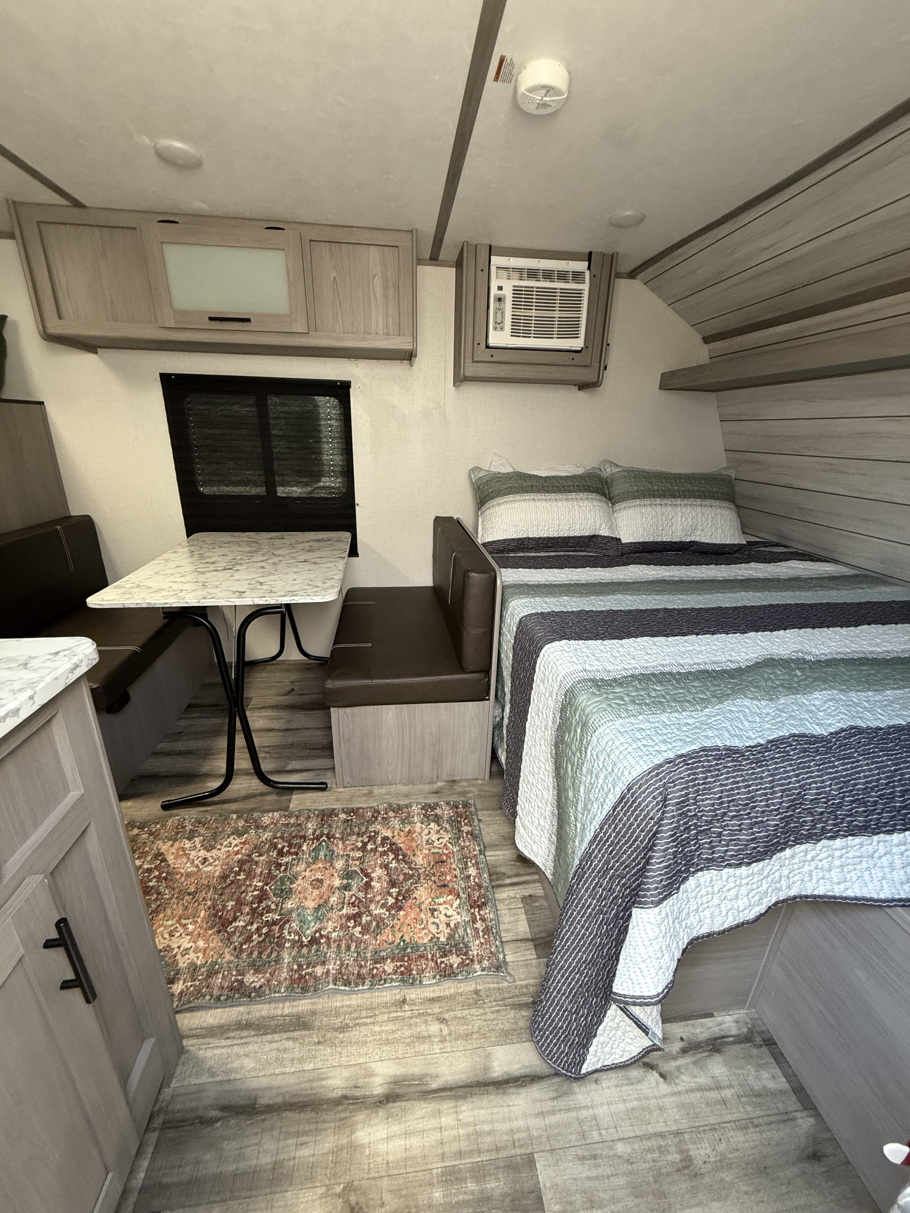 Explore this rv rental's compact interior: a comfy bed, dinette with table, overhead cabinets, and AC unit.. Dutchmen Coleman Lantern 2023