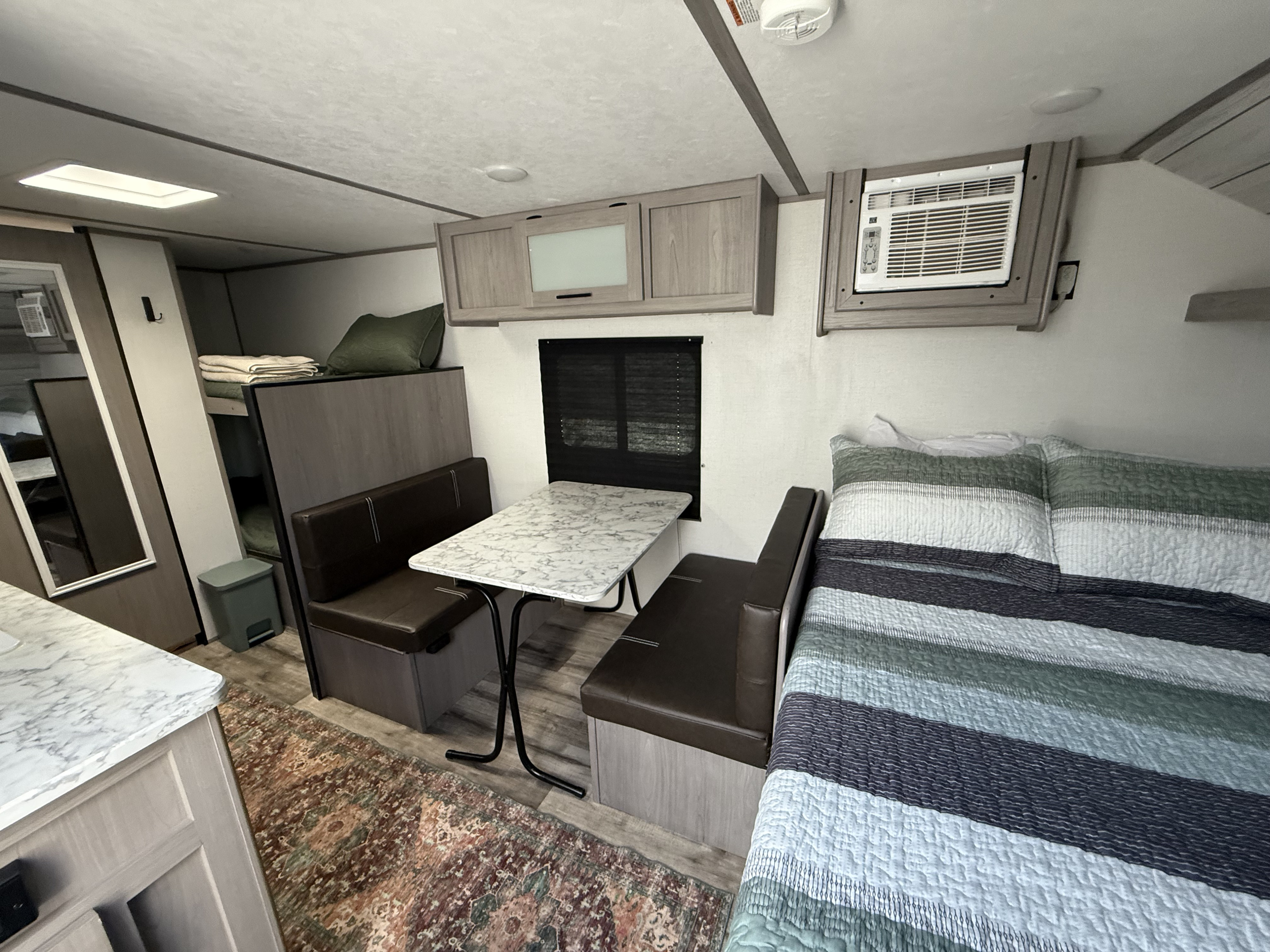 Cozy RV rental interior showing a dinette, bunk beds, main bed, and wall AC unit for a comfortable stay.. Dutchmen Coleman Lantern 2023