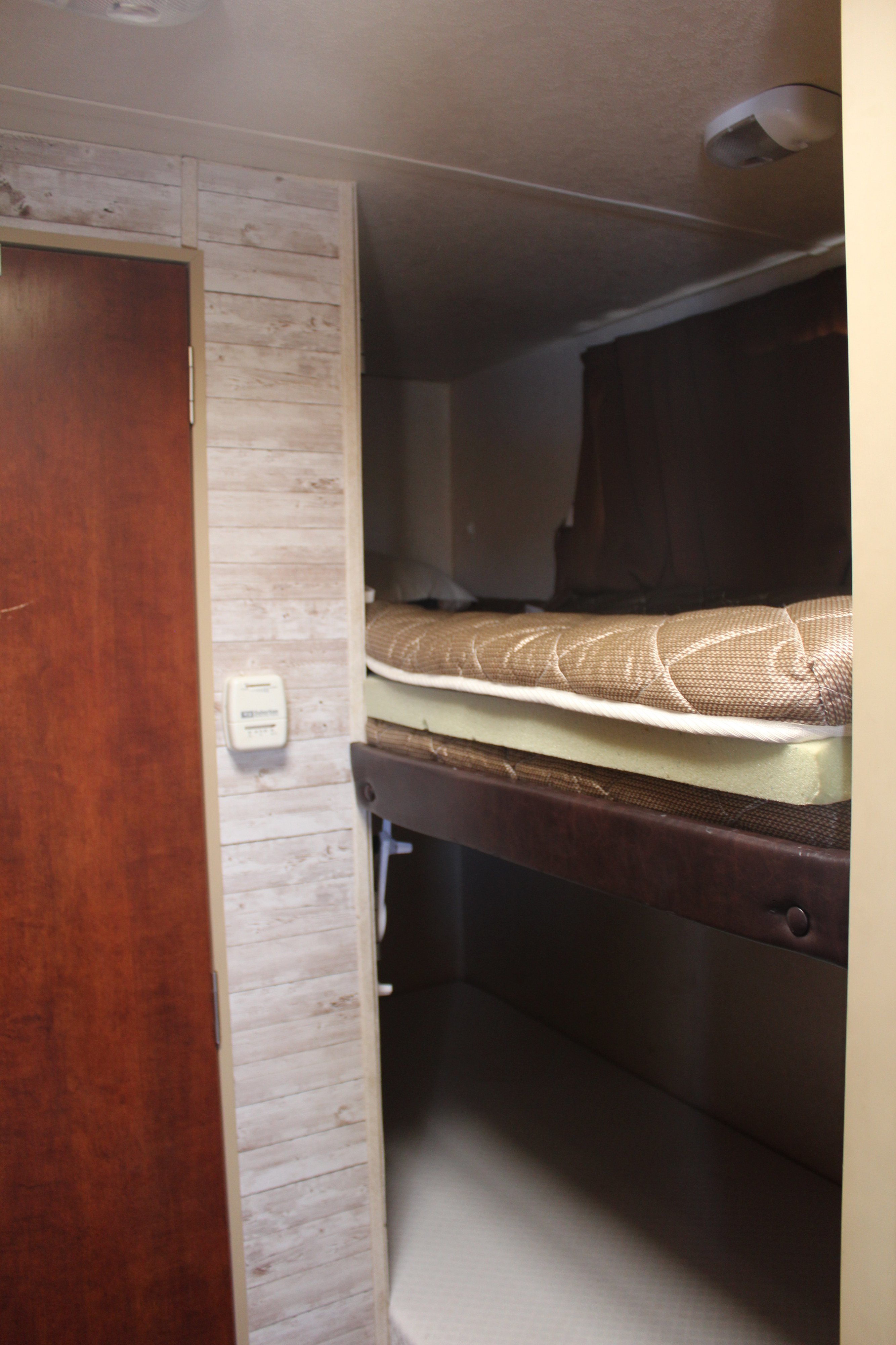 RV rental interior featuring comfortable bunk beds with mattress toppers, a wooden door, and thermostat.. Forest River Flagstaff E-Pro 2017