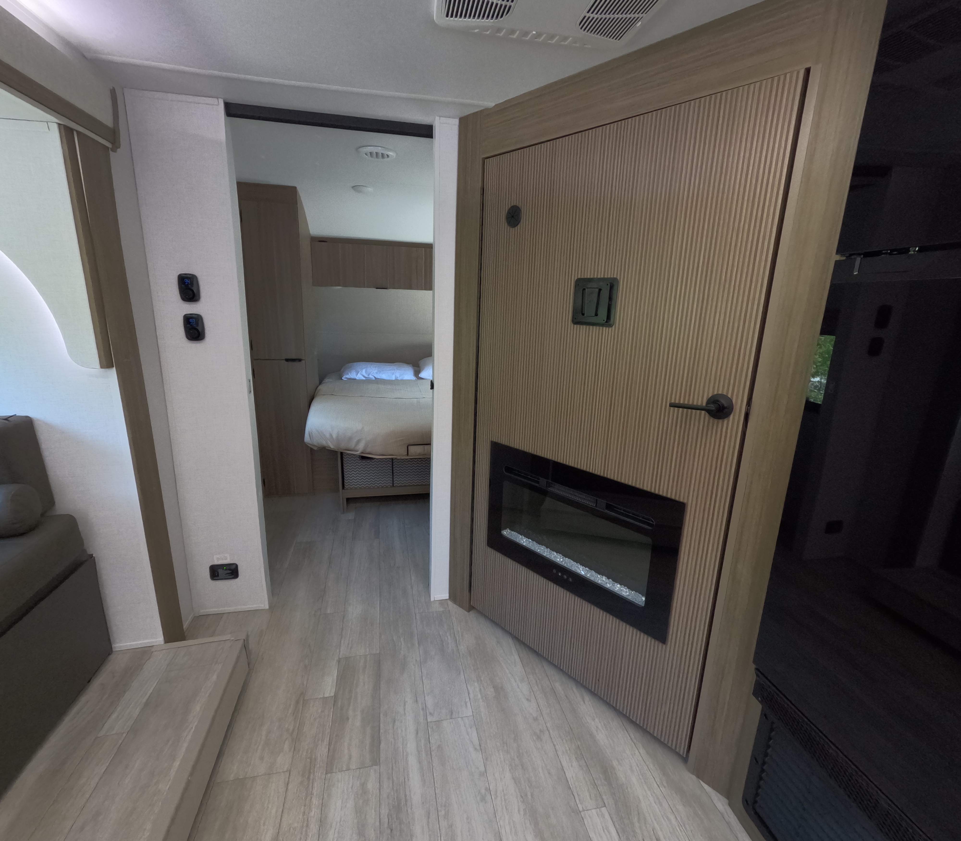 An RV rental's inviting interior, showcasing a cozy bedroom, a built-in fireplace, and modern light plank flooring.. Forest River Wildwood X-Lite 2025