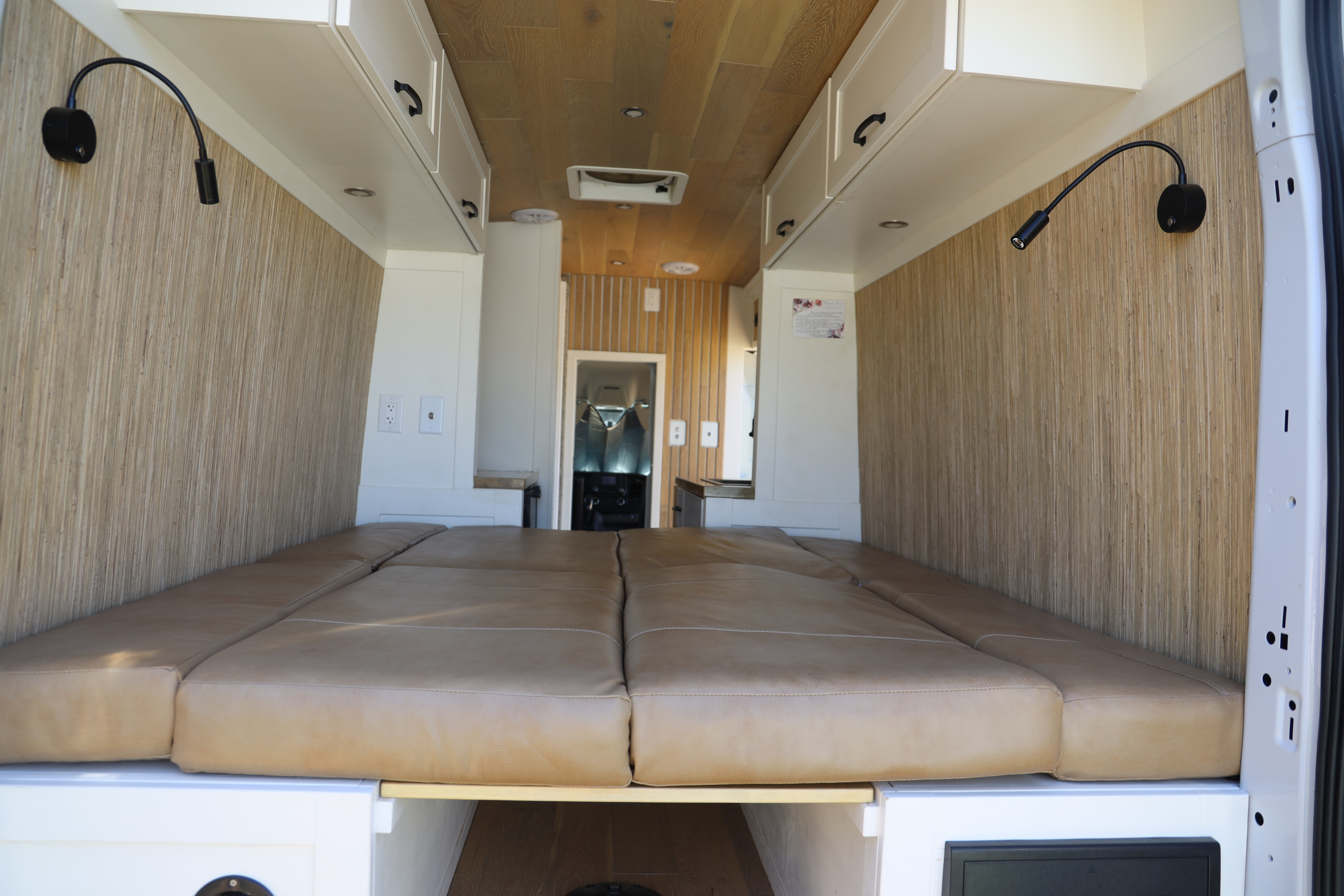 This RV rental offers a spacious camper van interior with a comfy bed, white cabinets, and stylish wooden paneling.. Ford Transit 2021