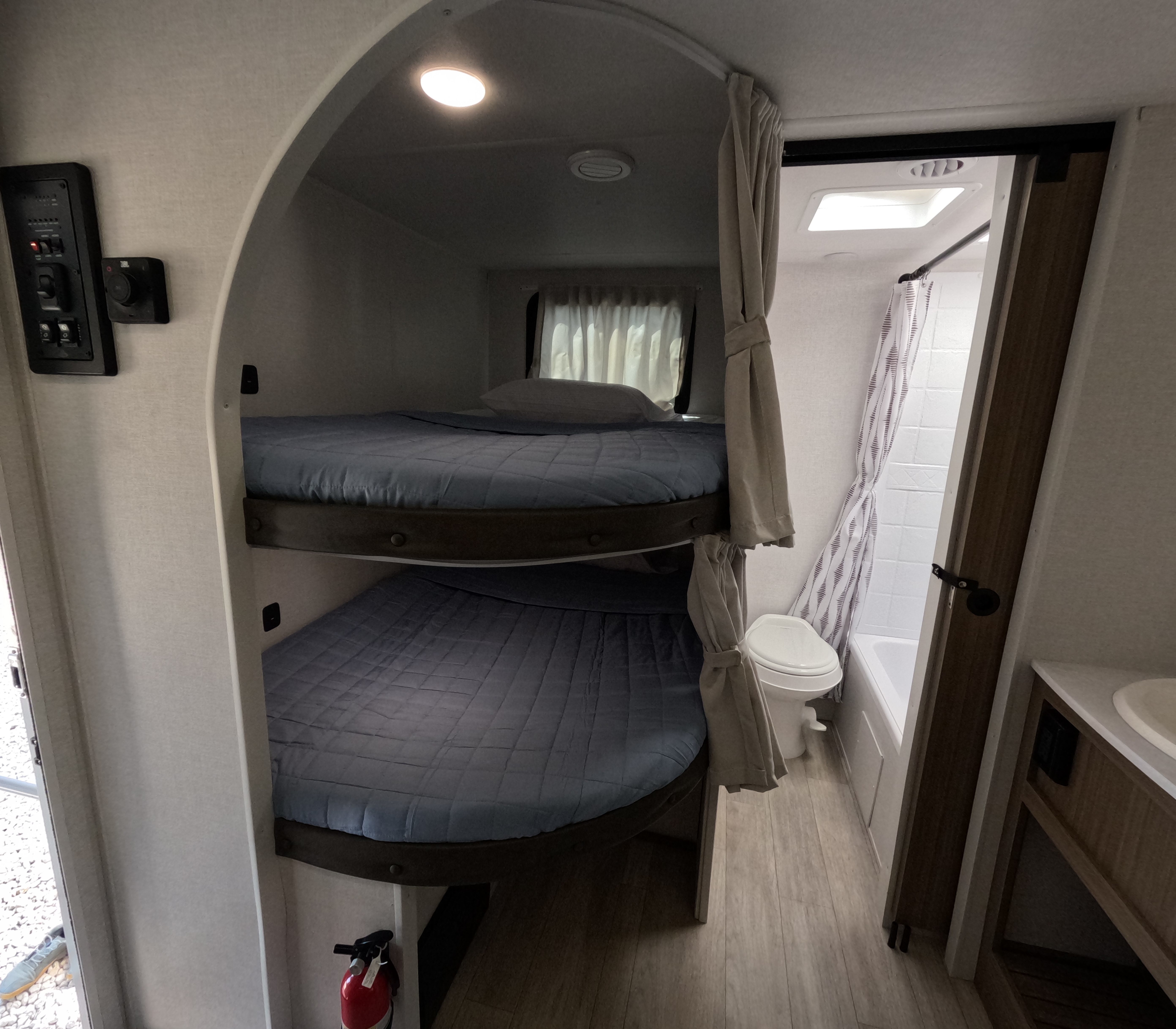 This RV rental offers cozy bunk beds with blue bedding, a compact bathroom with a toilet and shower, and essential controls.. Forest River Wildwood X-Lite 2025