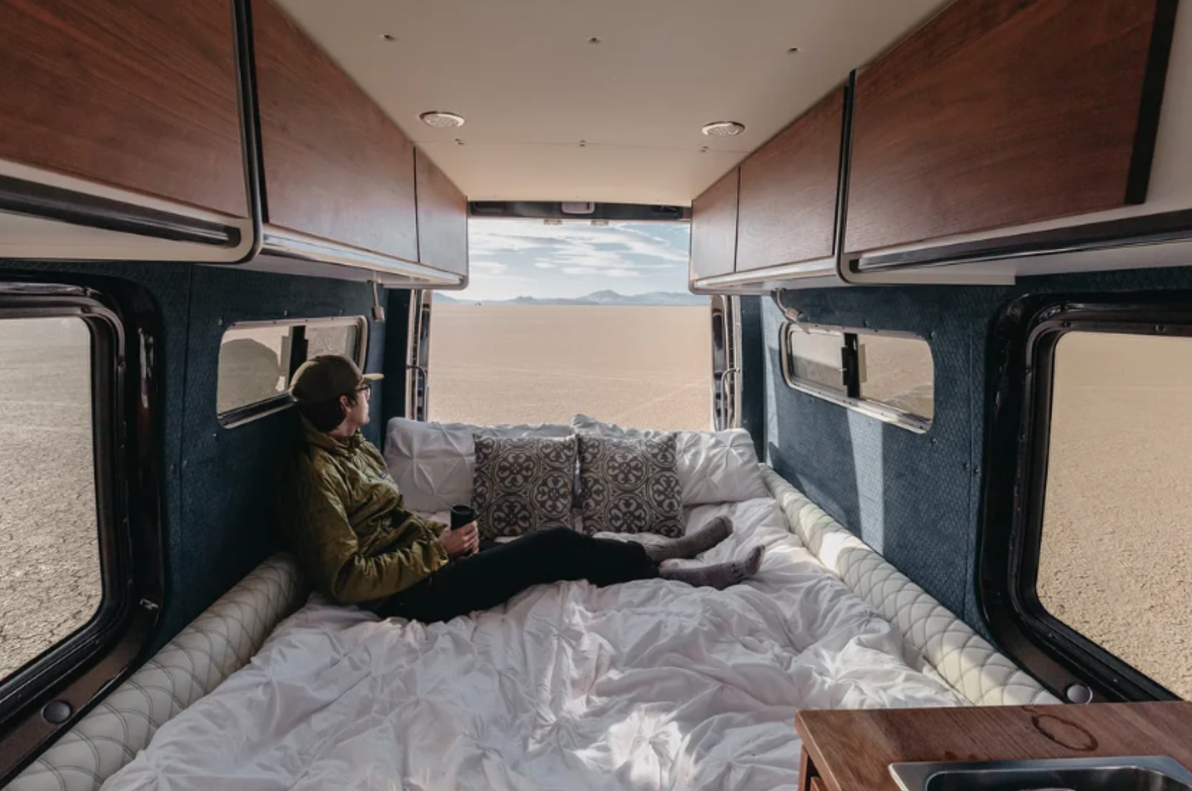 Enjoying a cozy rv rental, a person relaxes on a plush bed, gazing at the vast desert through the open van doors.. Mercedes-Benz Sprinter 2016