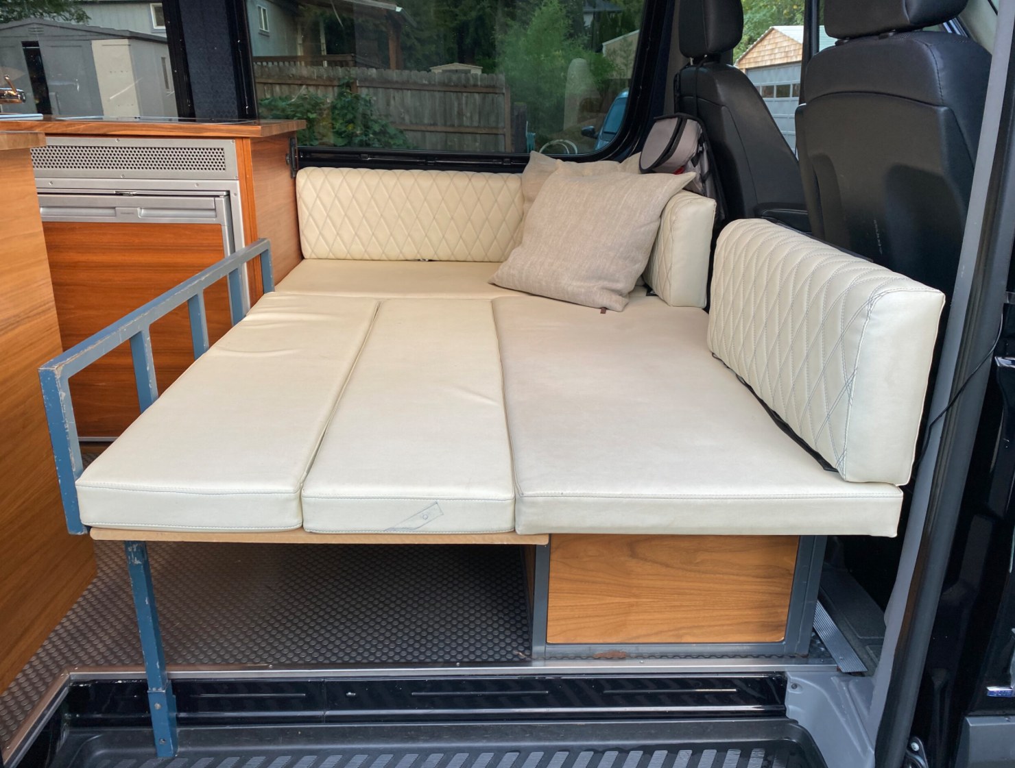 Inside this RV rental, a comfy modular bed/sofa with cream cushions, wood cabinets, and a built-in fridge.. Mercedes-Benz Sprinter 2016