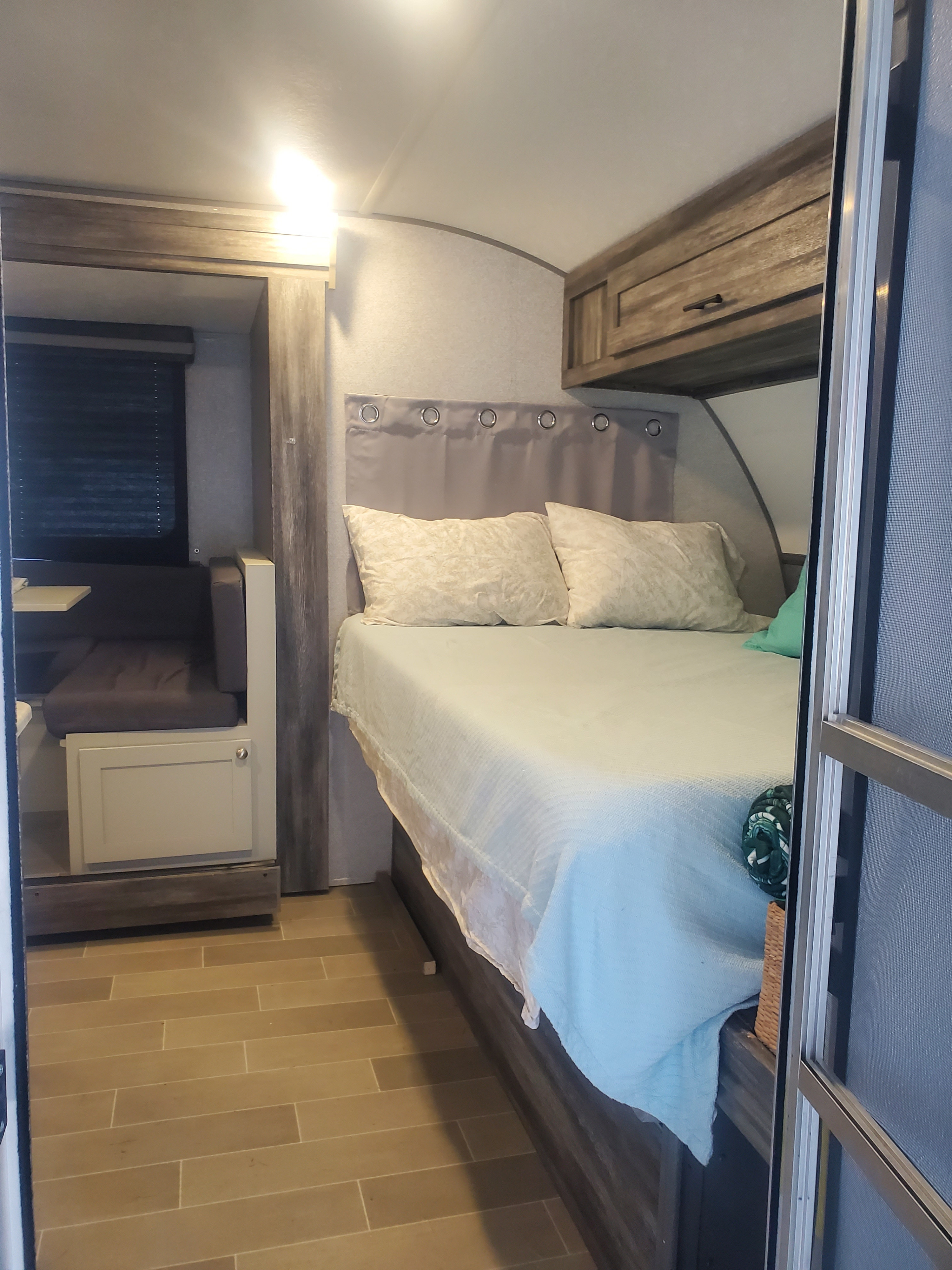 Inside an RV rental: A compact bedroom area with a bed, upholstered headboard, overhead cabinets, and a dinette to the left.. Forest River Wildwood FSX Platinum 2020