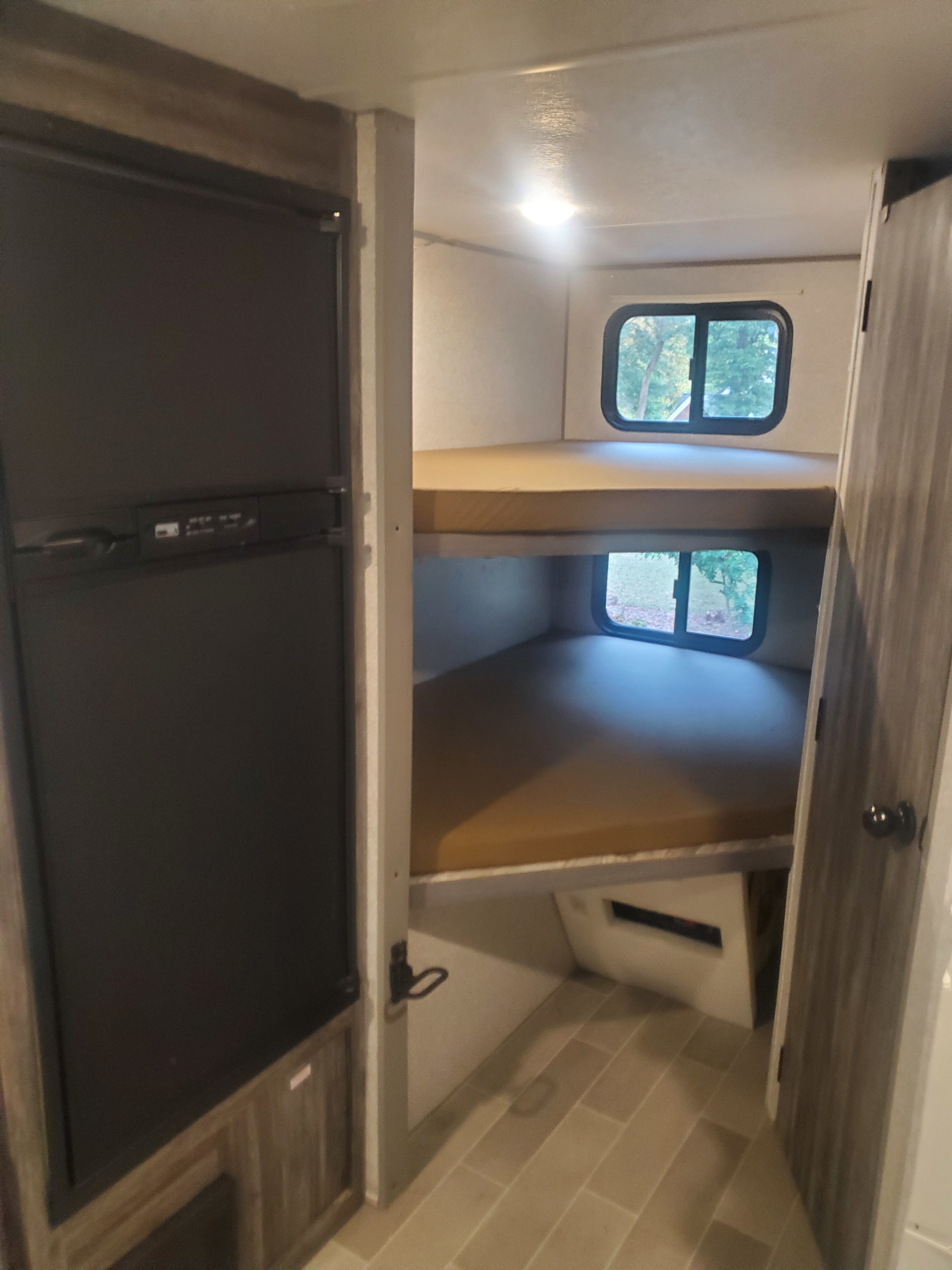 RV rental interior: Bunk beds with windows and a refrigerator on the left, offering a compact sleeping area.. Forest River Wildwood FSX Platinum 2020