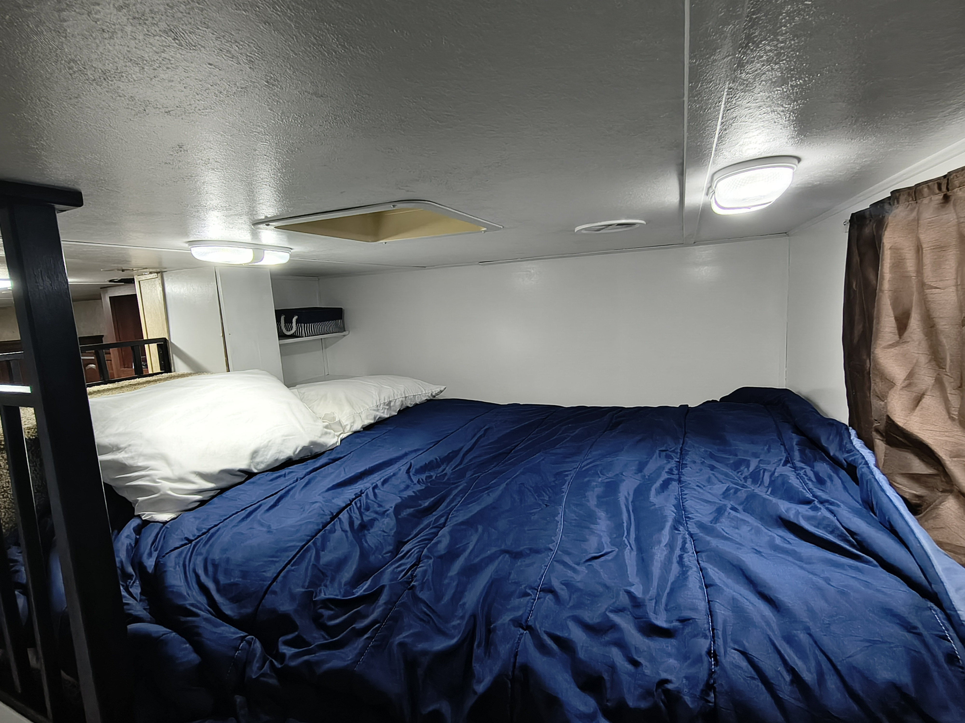 Cozy RV rental bunk bed with blue comforter, white pillows, and overhead lighting, offering a comfortable sleeping space.. Forest River Salem Hemisphere Lite 2012