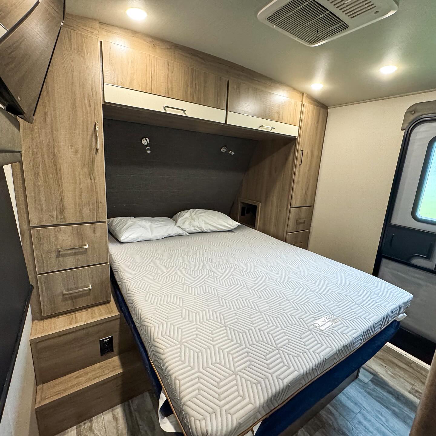 RV rental interior: A cozy bedroom with a patterned mattress, ample storage cabinets, and an AC unit for comfort.. Grand Design Imagine 2022