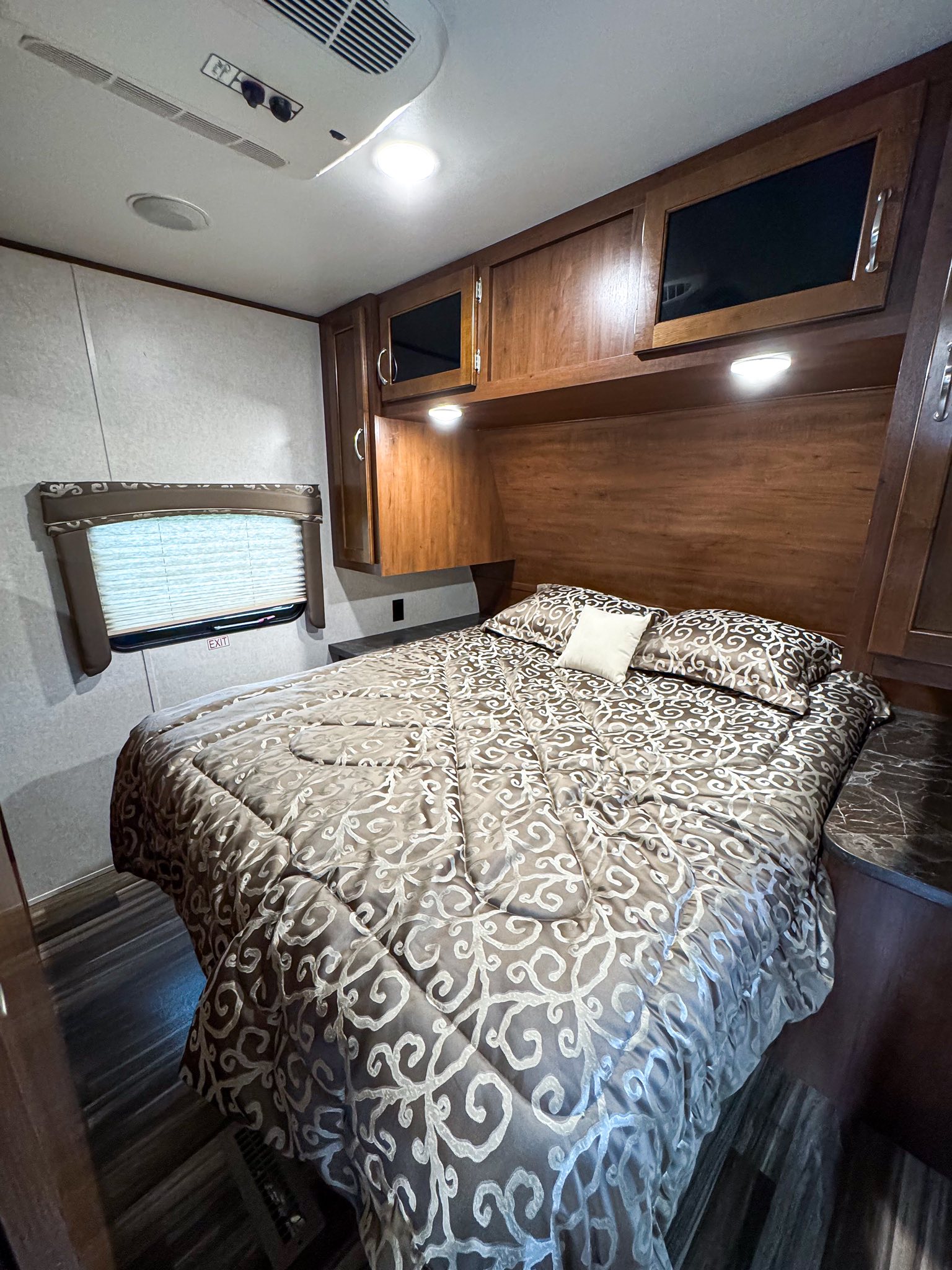 Inviting RV rental bedroom: patterned bed, wooden overhead cabinets, window, ceiling AC. Cozy, compact mobile travel space.. Jayco Jay Flight 2017