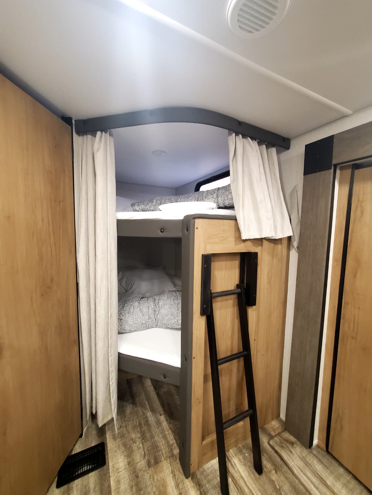 Cozy RV rental bunk beds with privacy curtains and a ladder, offering a comfortable sleeping area for family adventures.. Forest River WOLF DEN 2024