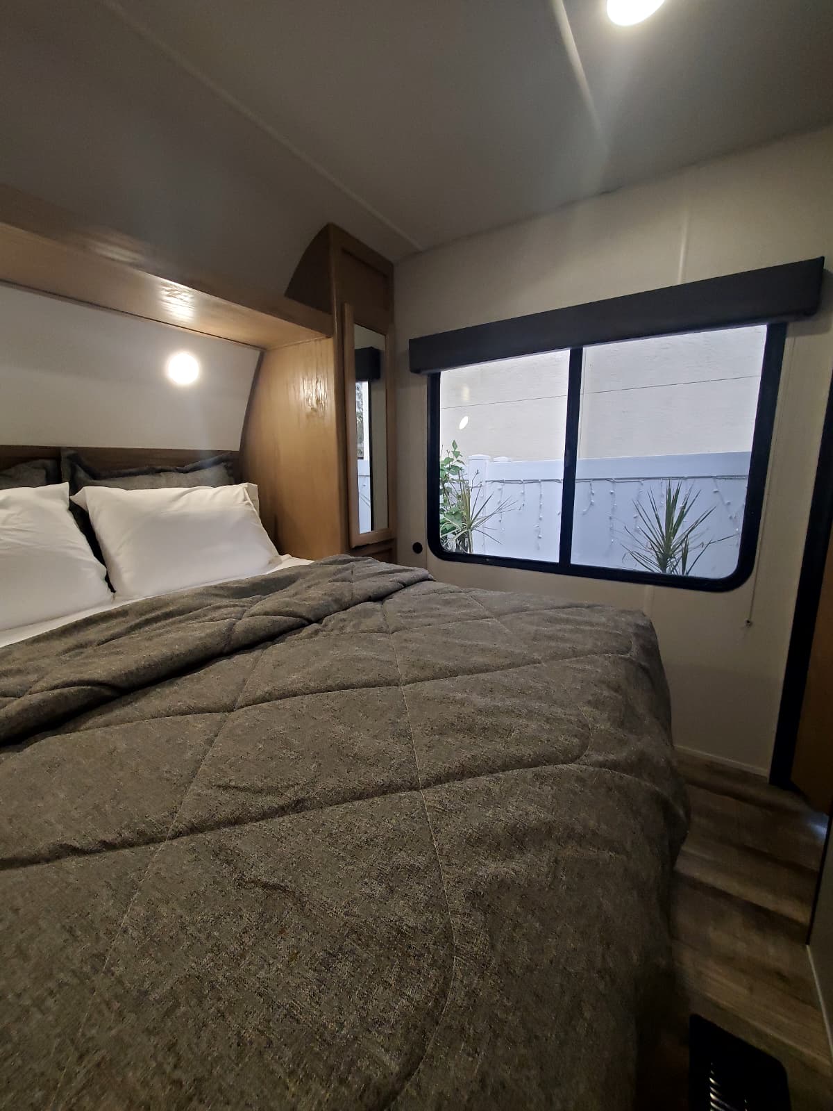 A comfortable RV rental bedroom features a neatly made bed with a gray comforter and white pillows, plus a window.. Forest River WOLF DEN 2024