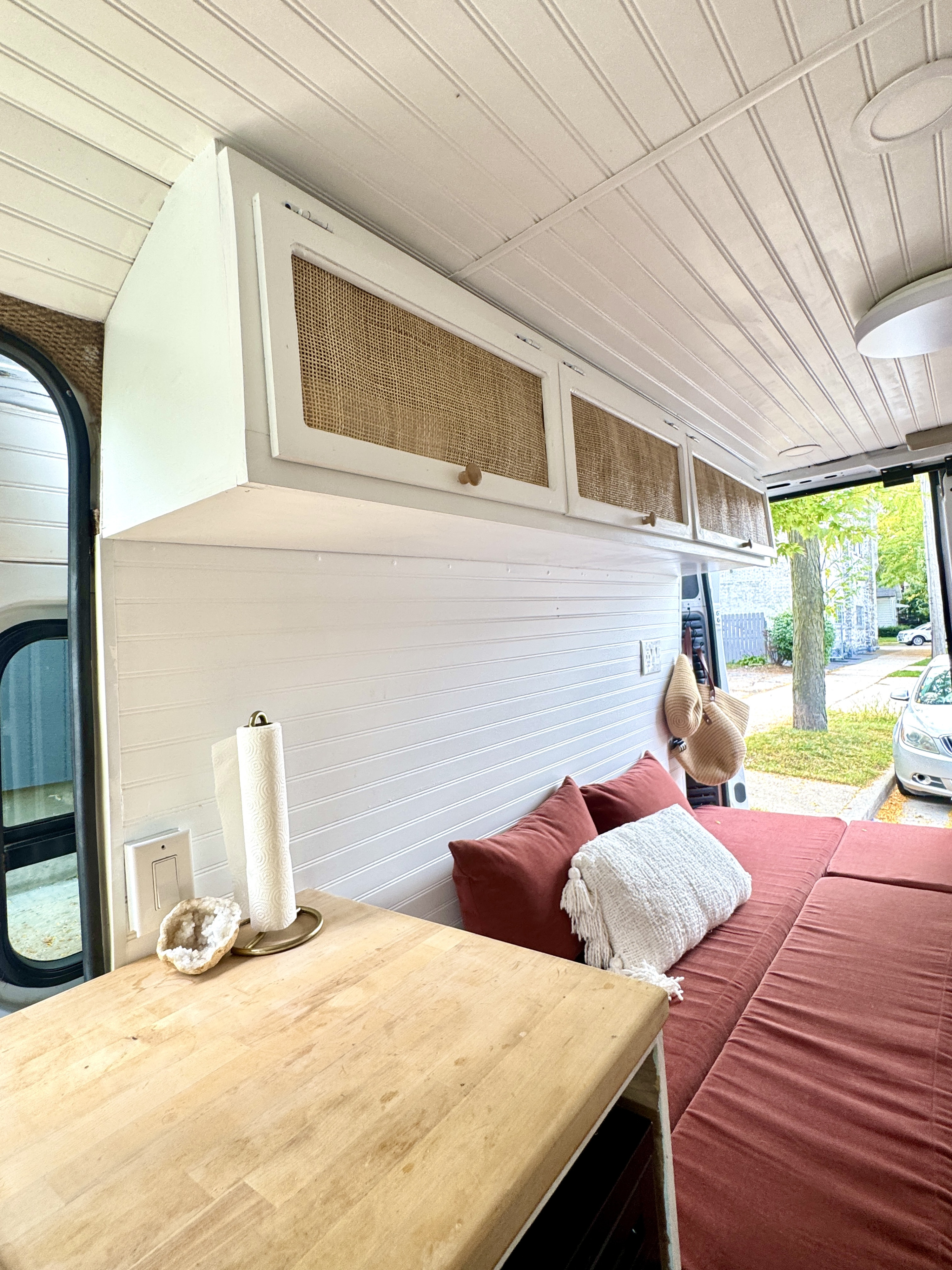 This RV rental's cozy interior features custom overhead cabinets, a wooden table, and inviting red cushions for comfortable travel.. Dodge Promaster 2019