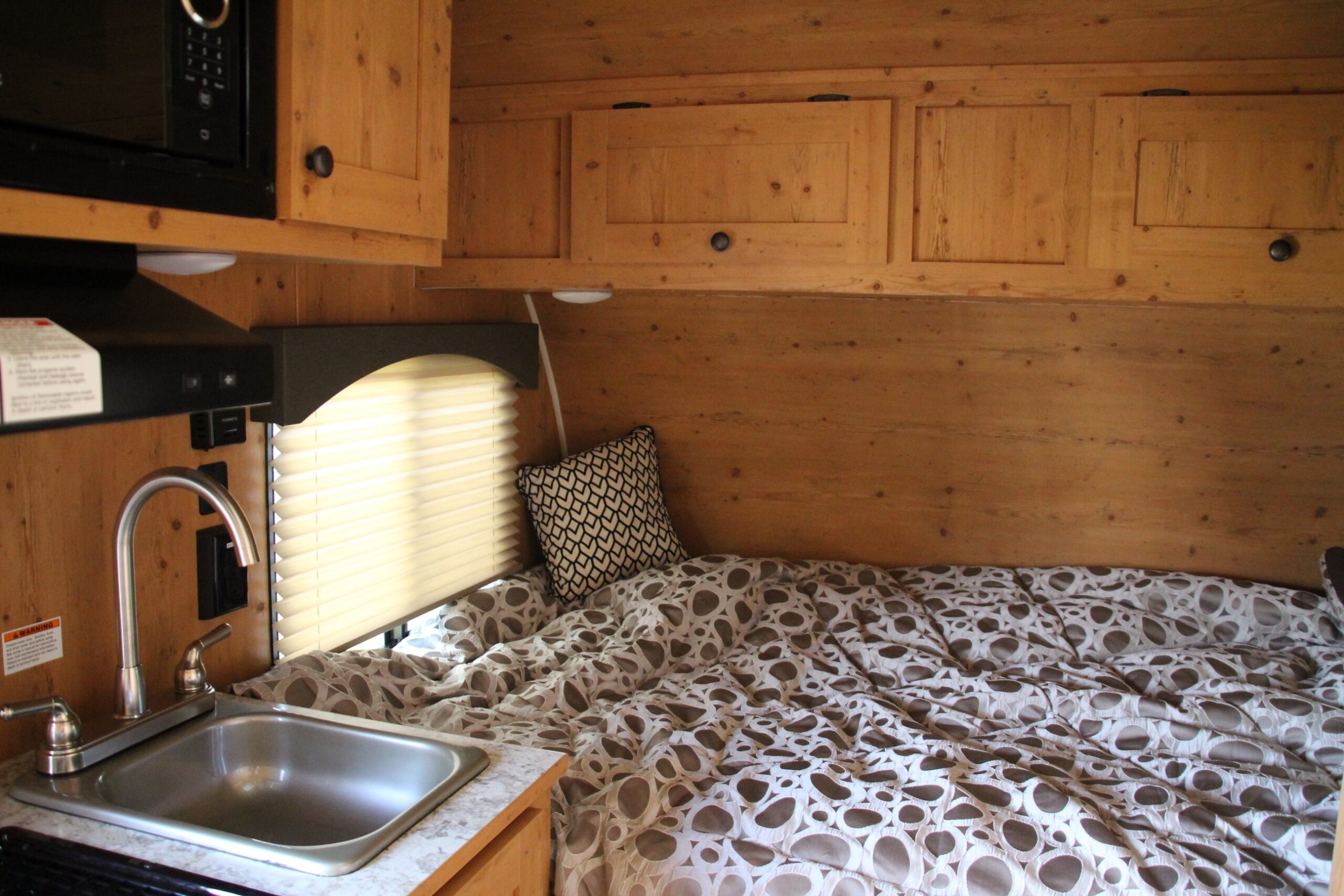 Cozy RV rental interior showcasing a compact kitchen with sink and microwave, alongside a comfortable bed with patterned bedding and wooden accents.. Sunray Sport 149 2021