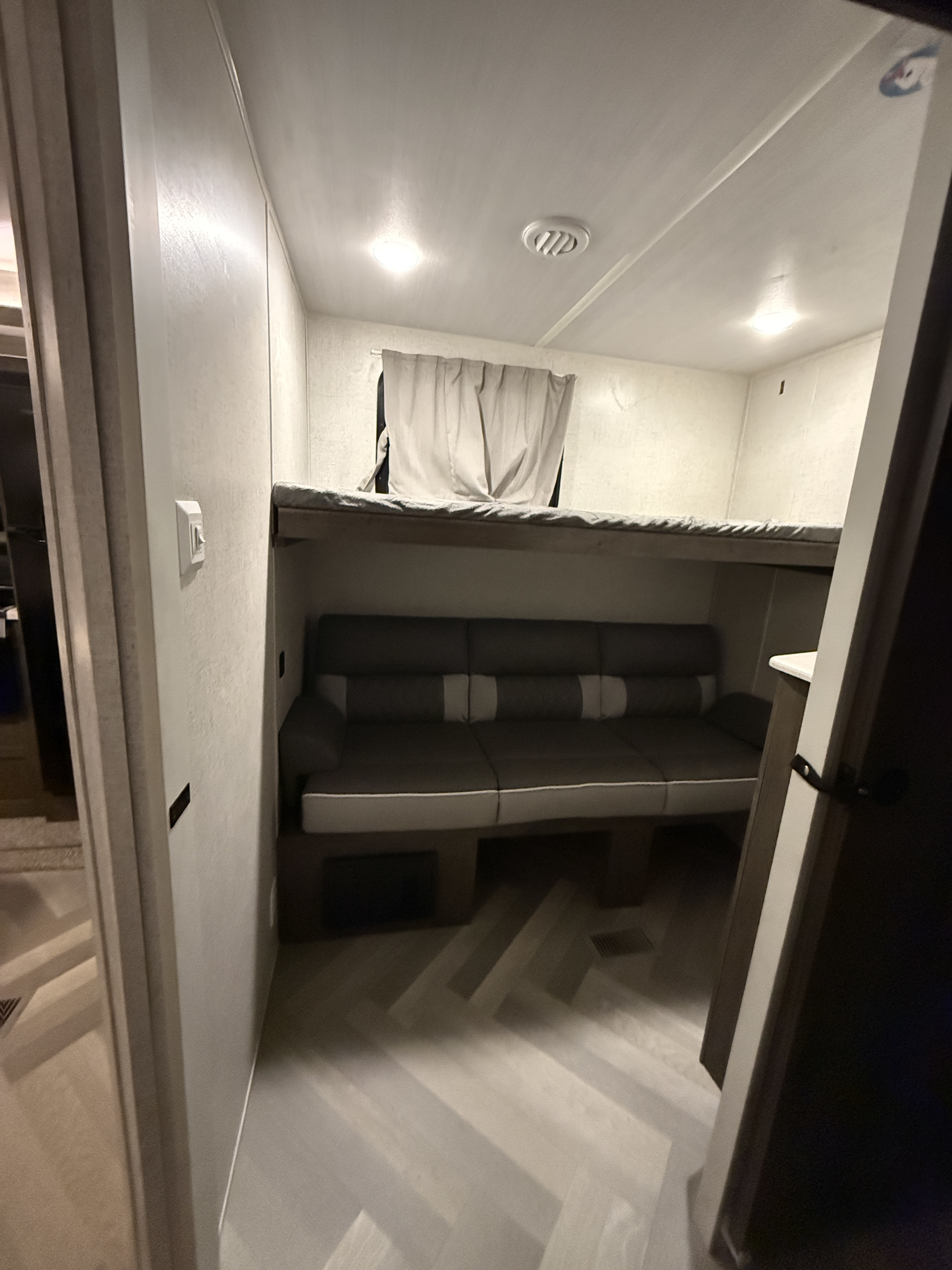 Cozy RV rental bunk area: a lower sofa converts for sleeping, with an upper bunk, window, and modern herringbone flooring.. Forest River Salem 2021