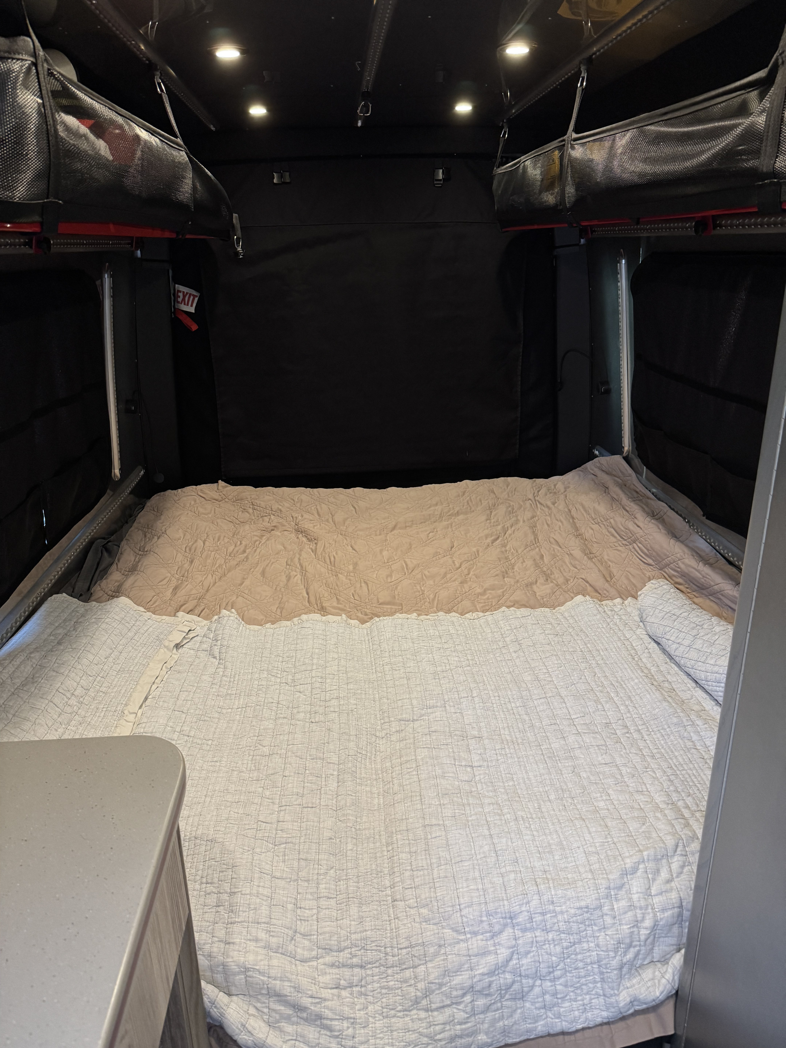 Cozy RV rental bedroom with quilted bed, overhead lights, exit sign, and mesh storage netting.. Airstream Interstate 2023