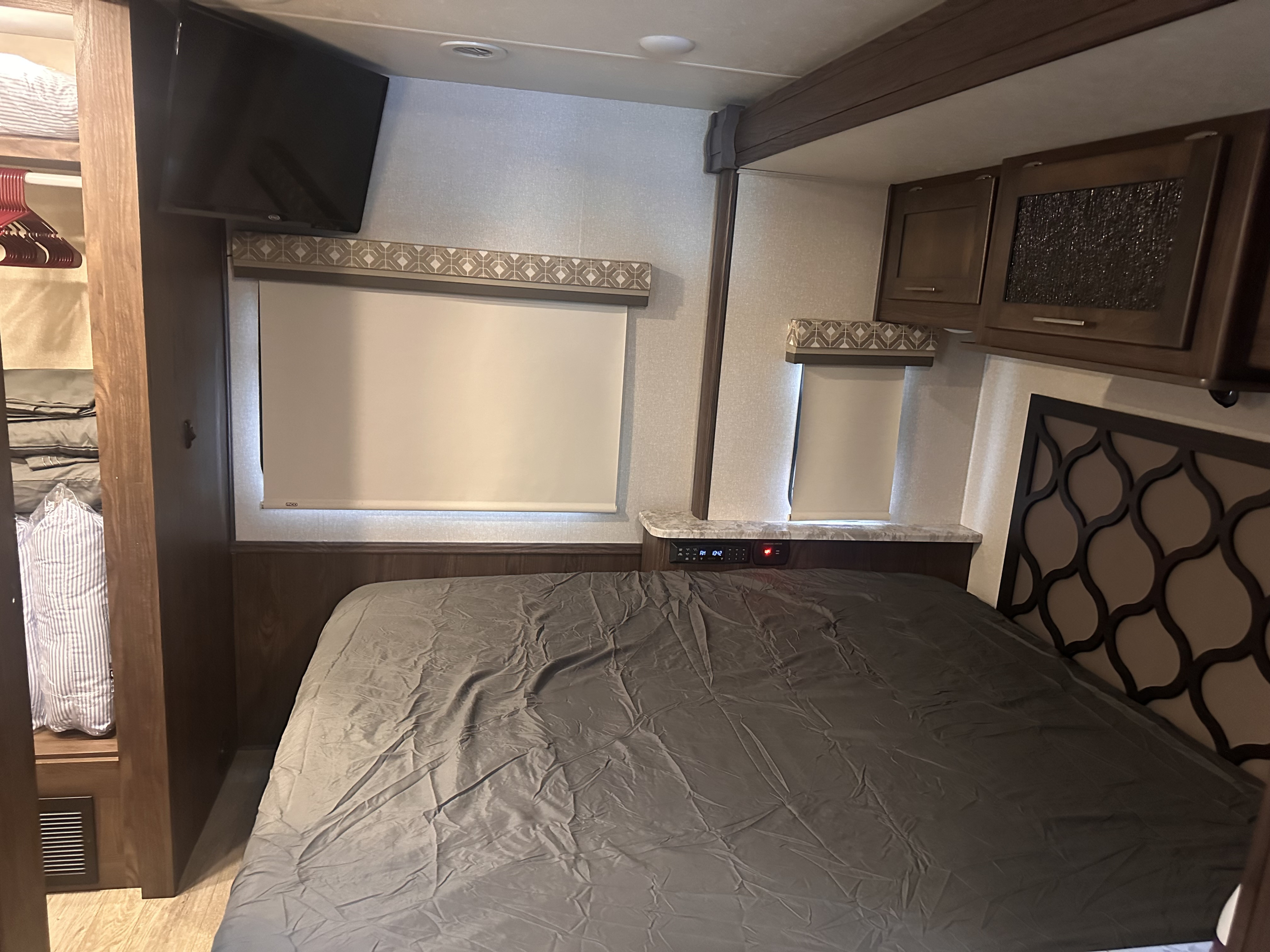 This RV rental bedroom features a bed, wall-mounted TV, storage, and closet, offering a compact and functional living space.. Coachman Pursuit 2020