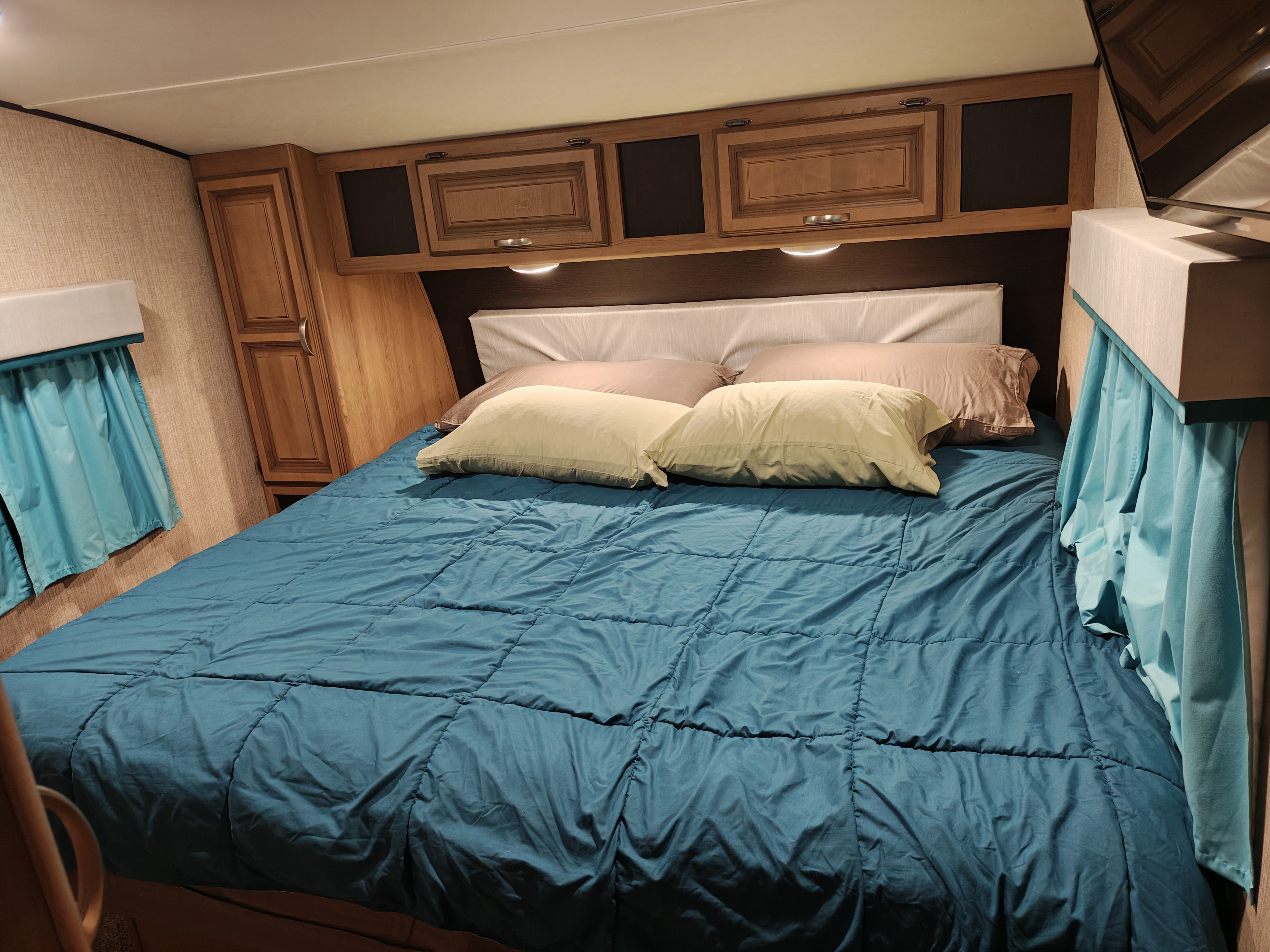 RV rental bedroom featuring a comfortable bed with a blue comforter, pillows, and functional overhead cabinets.. Crossroads RV Cruiser Aire 2017